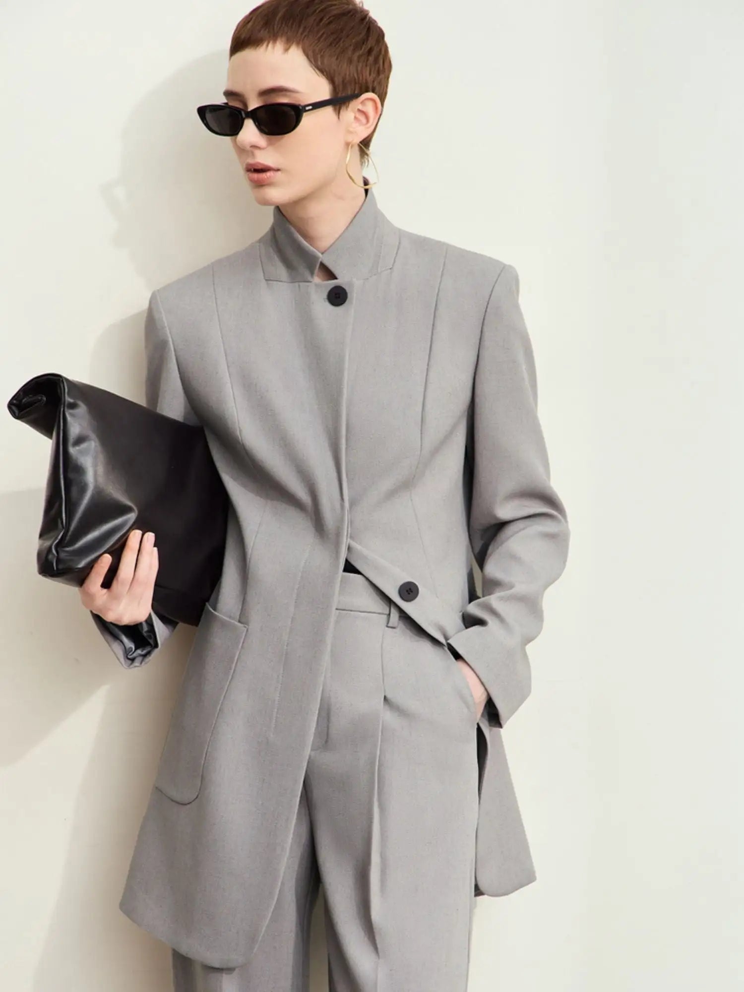 Person wearing a gray suit holding a black clutch against a white background