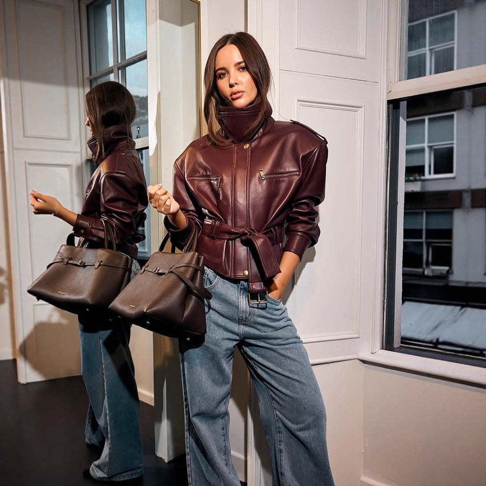 Women's short jacket made of faux leather with a high stand-up collar, fitted tie belt, and prominent shoulder pads Chichicherry