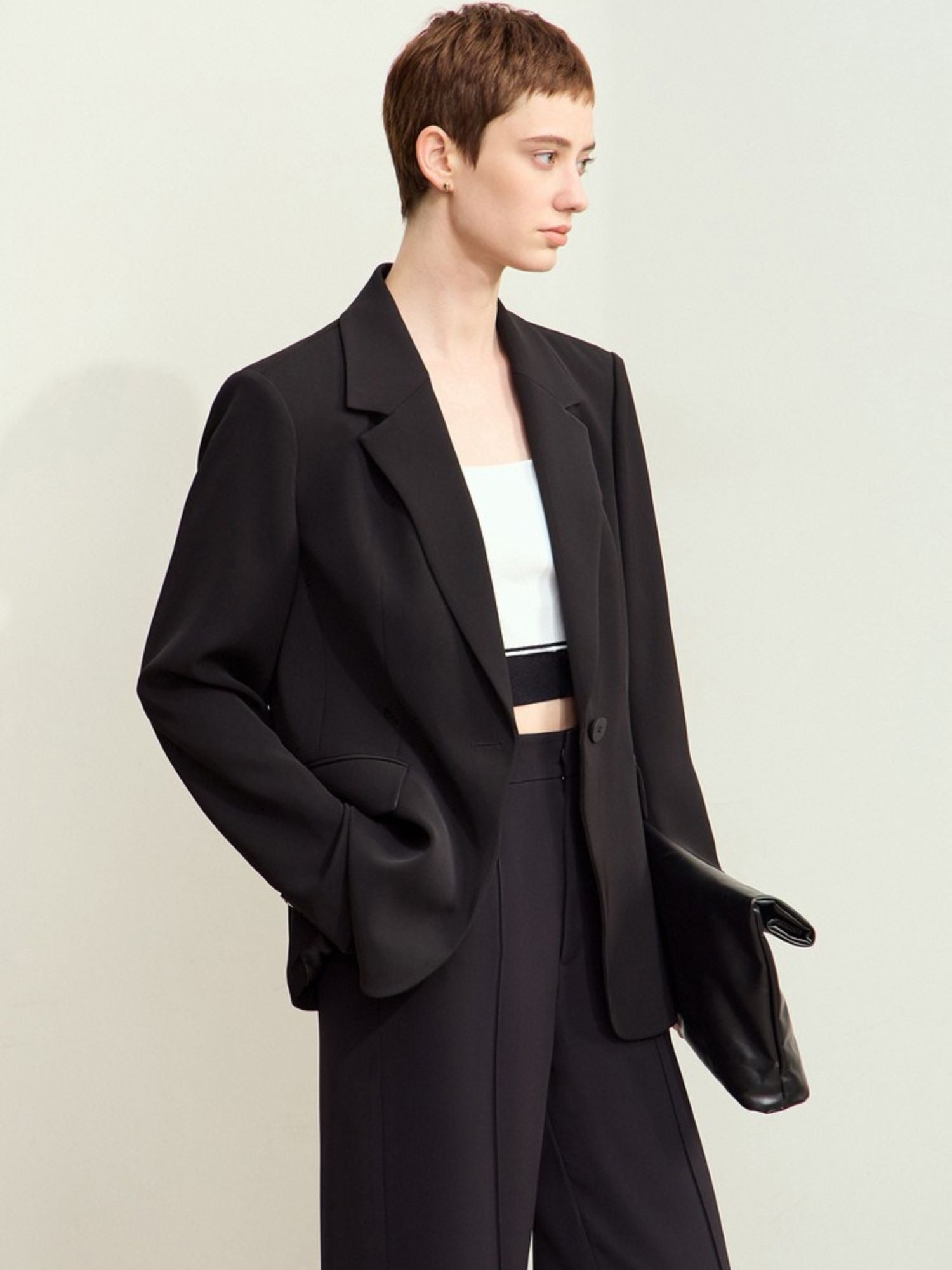 Side view of black blazer paired with matching trousers and black handbag