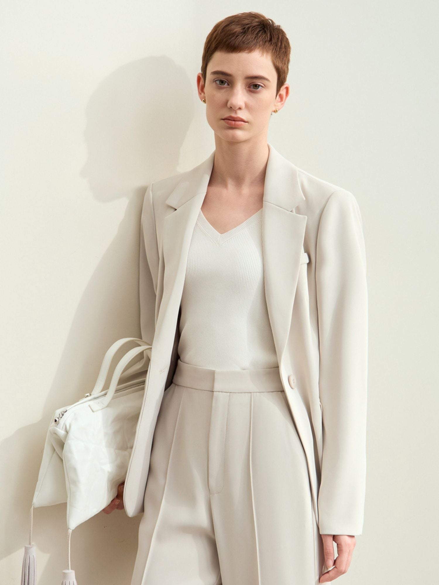 Front view of cream blazer styled with trousers and white handbag