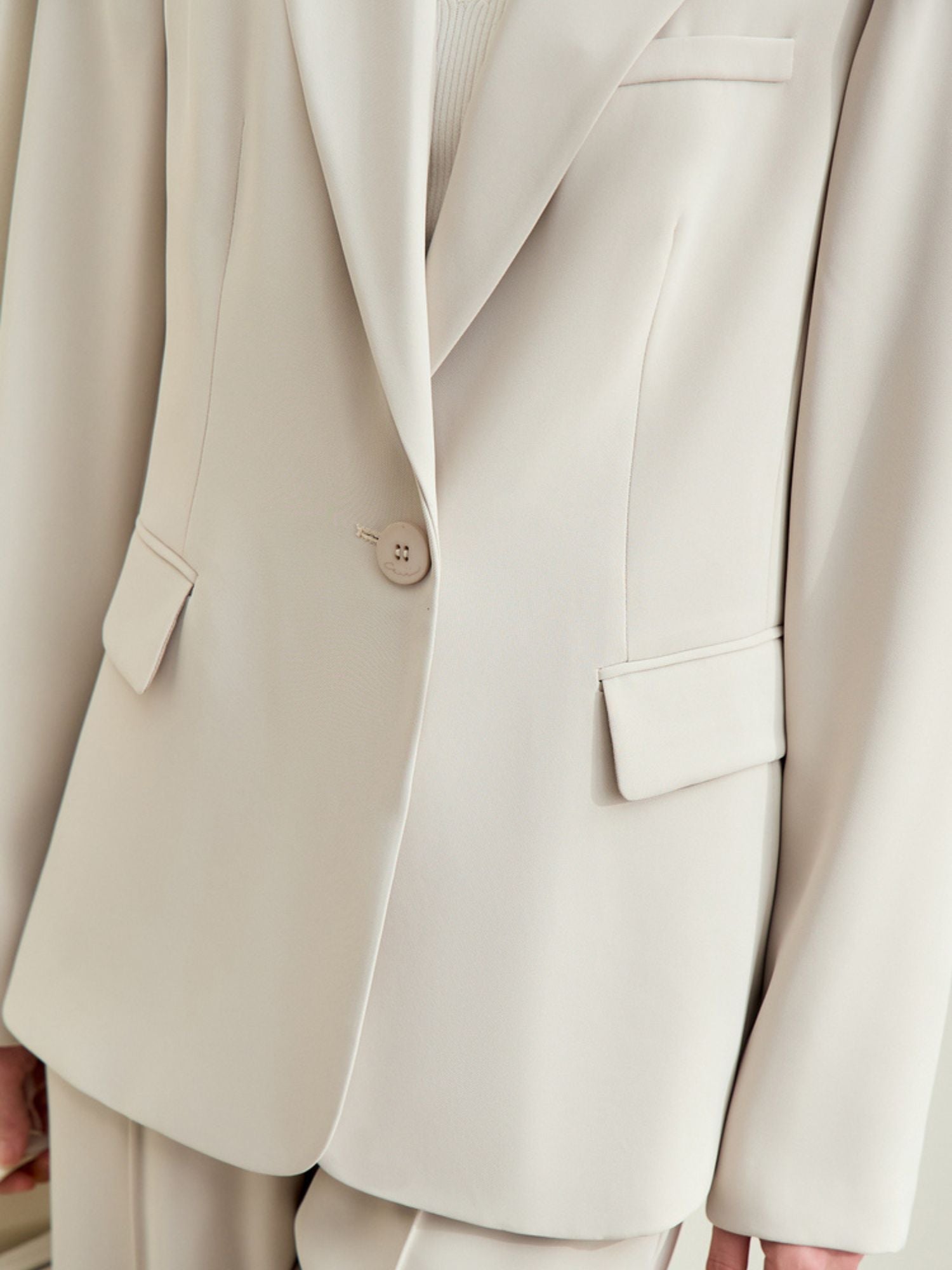Close up front view of cream blazer showing single-button front and flap pockets.