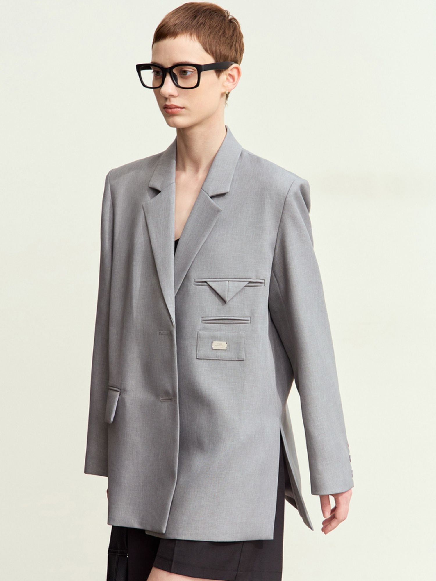 Close-up of light grey blazer flap pocket with subtle welt stitching and model wearing glasses
