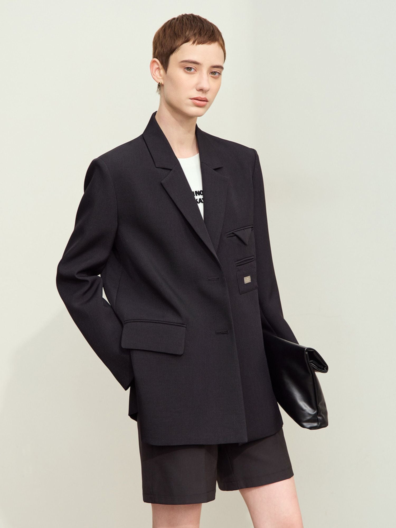 Model wearing black oversized double‑breasted blazer styled with shorts and clutch