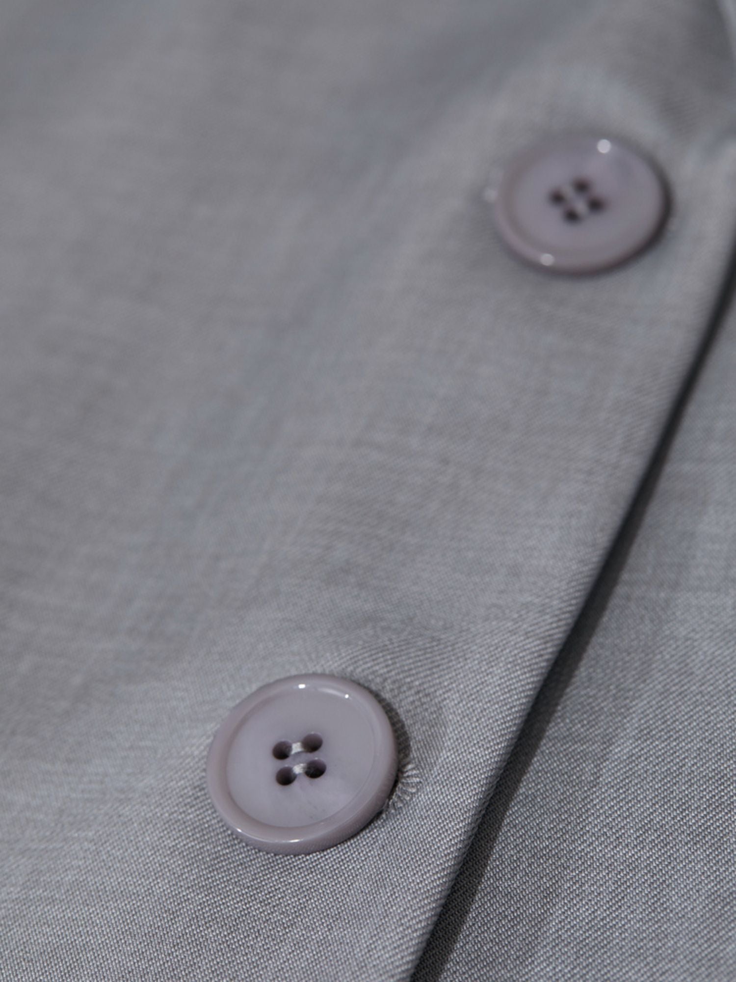 Close-up of two grey buttons on light blazer sleeve emphasizing tonal stitching