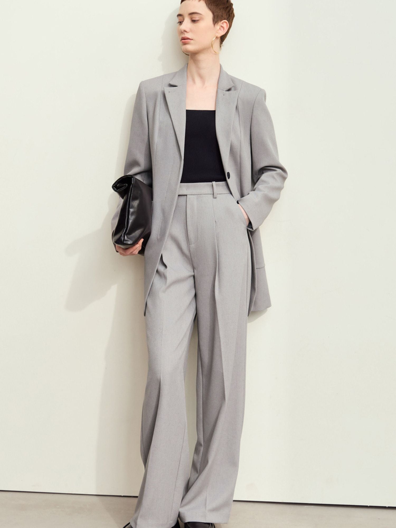 Full-body view: model in light-grey blazer with matching trousers and clutch