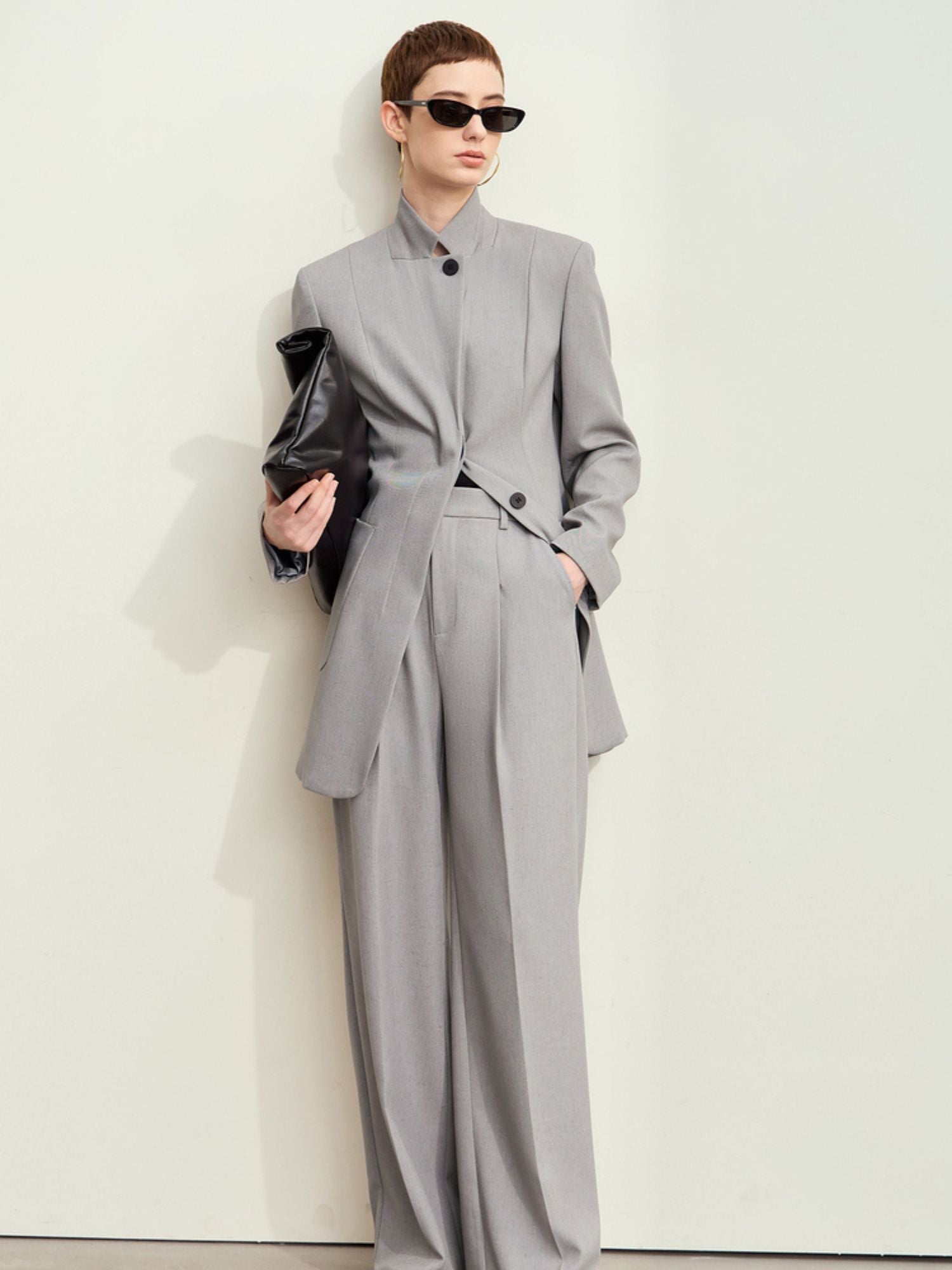 Full-body view: model in light-grey blazer with matching trousers and black clutch