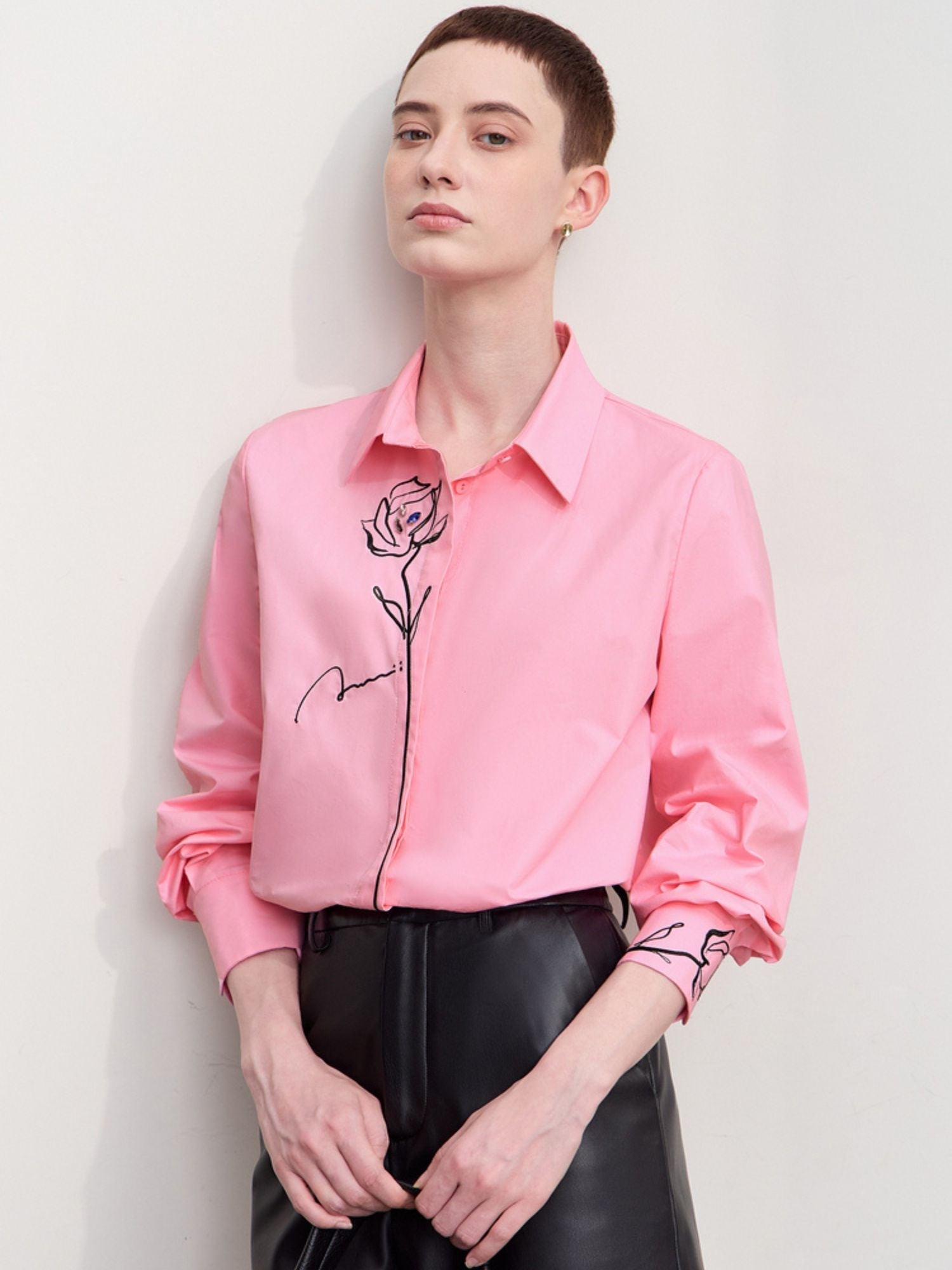 Model wearing pink version of the rose‑embroidered shirt paired with black shorts and holding a bag