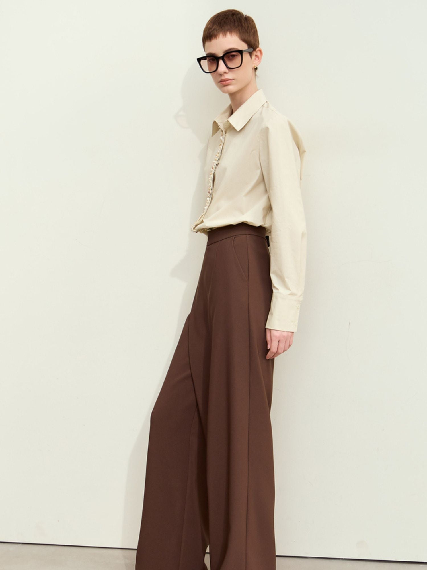 Full view of the model wearing sheer beige long-sleeve blouse, paired with trousers