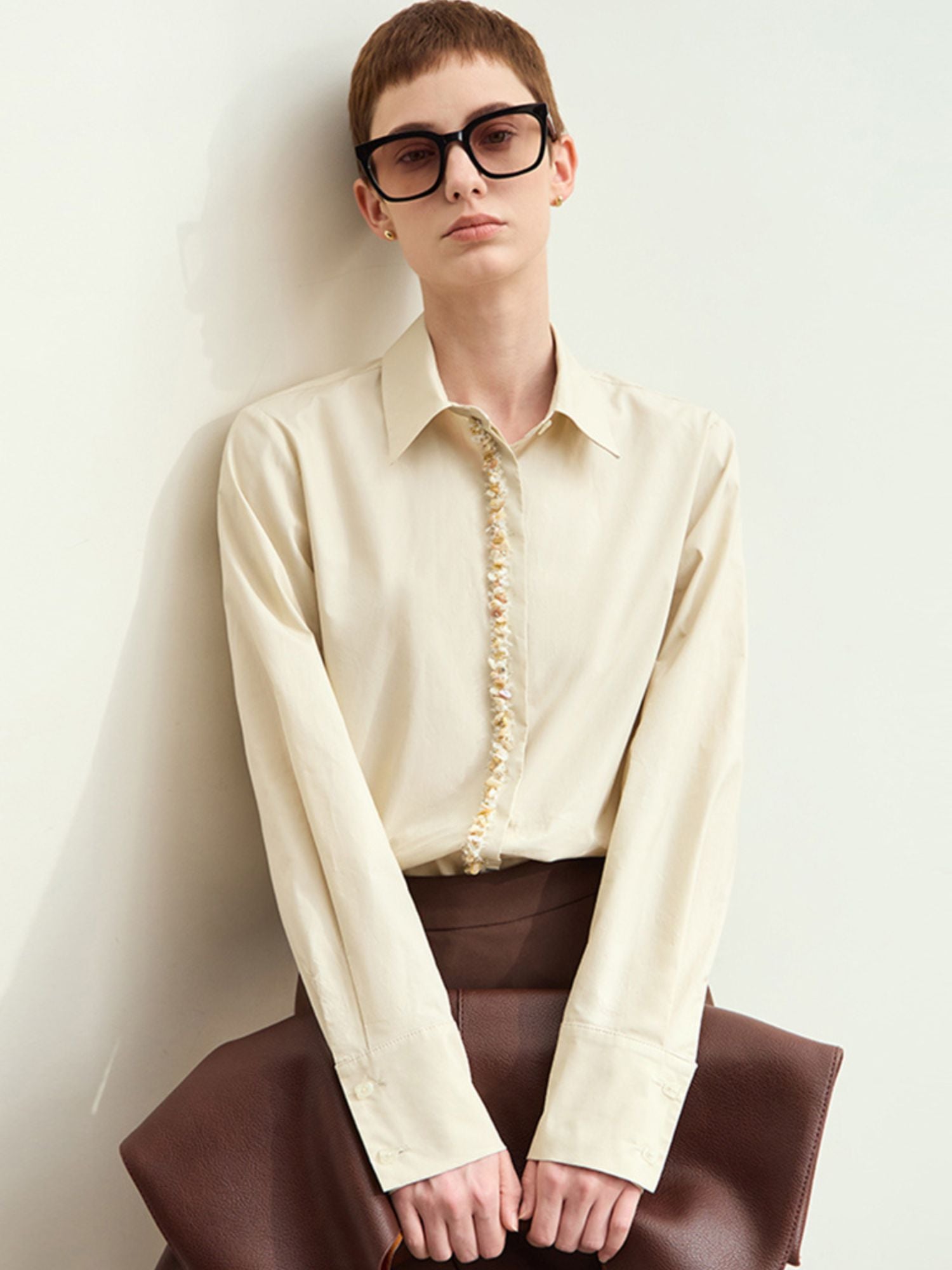 Model wearing beige long-sleeve blouse top tucked into jeans, clutch at side, front view.