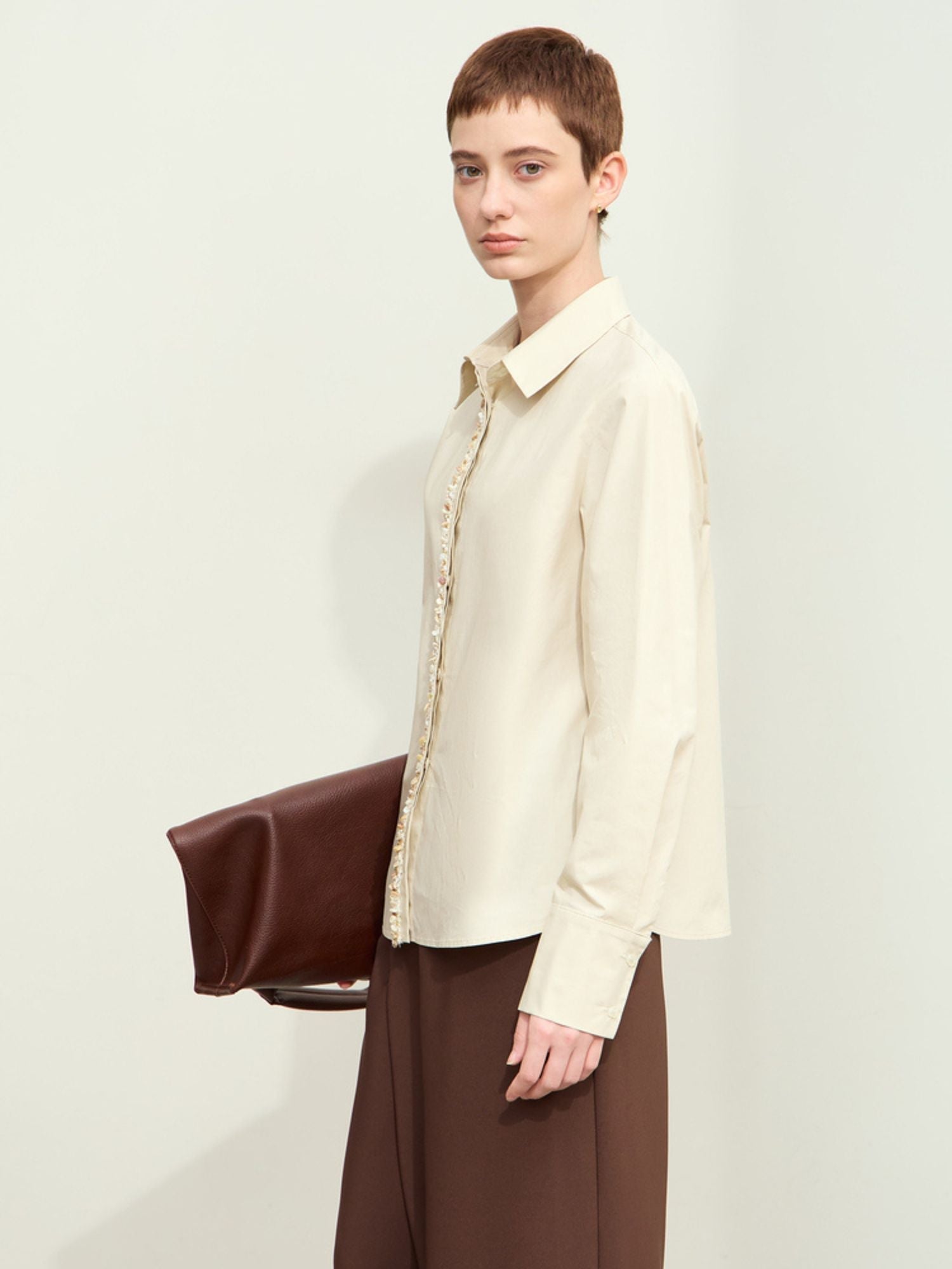 Side view of model in beige long sleeves blouse holding a brown clutch