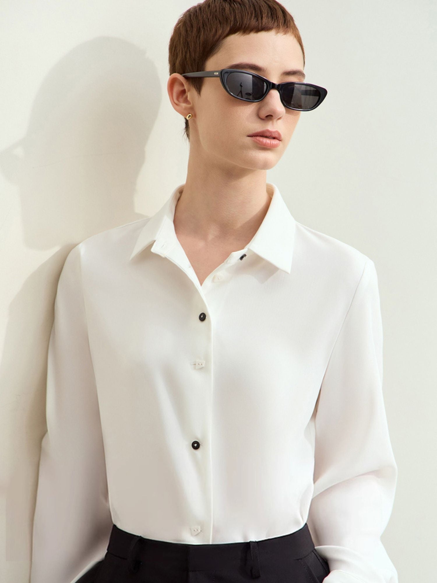 Model wearing white silk blouse and black trousers, front view with minimalist styling