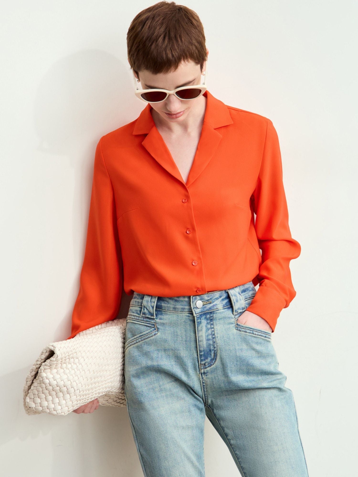 Model wearing rust-orange silk blouse with pointed collar tucked into charcoal trousers and styled with a handbag