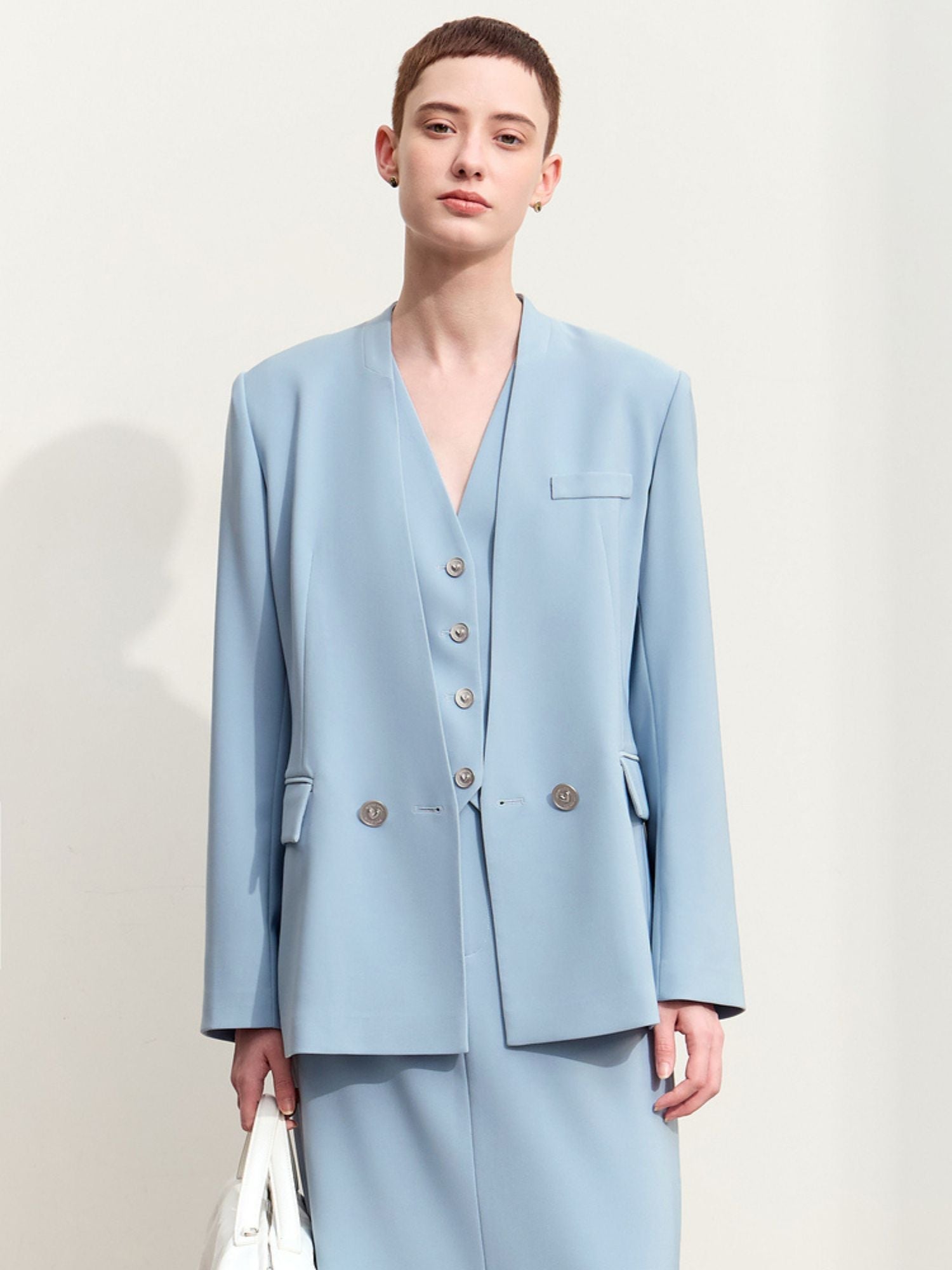 Front view of the light blue double-breasted blazer with structured shoulders and silver hardware with a white handbag