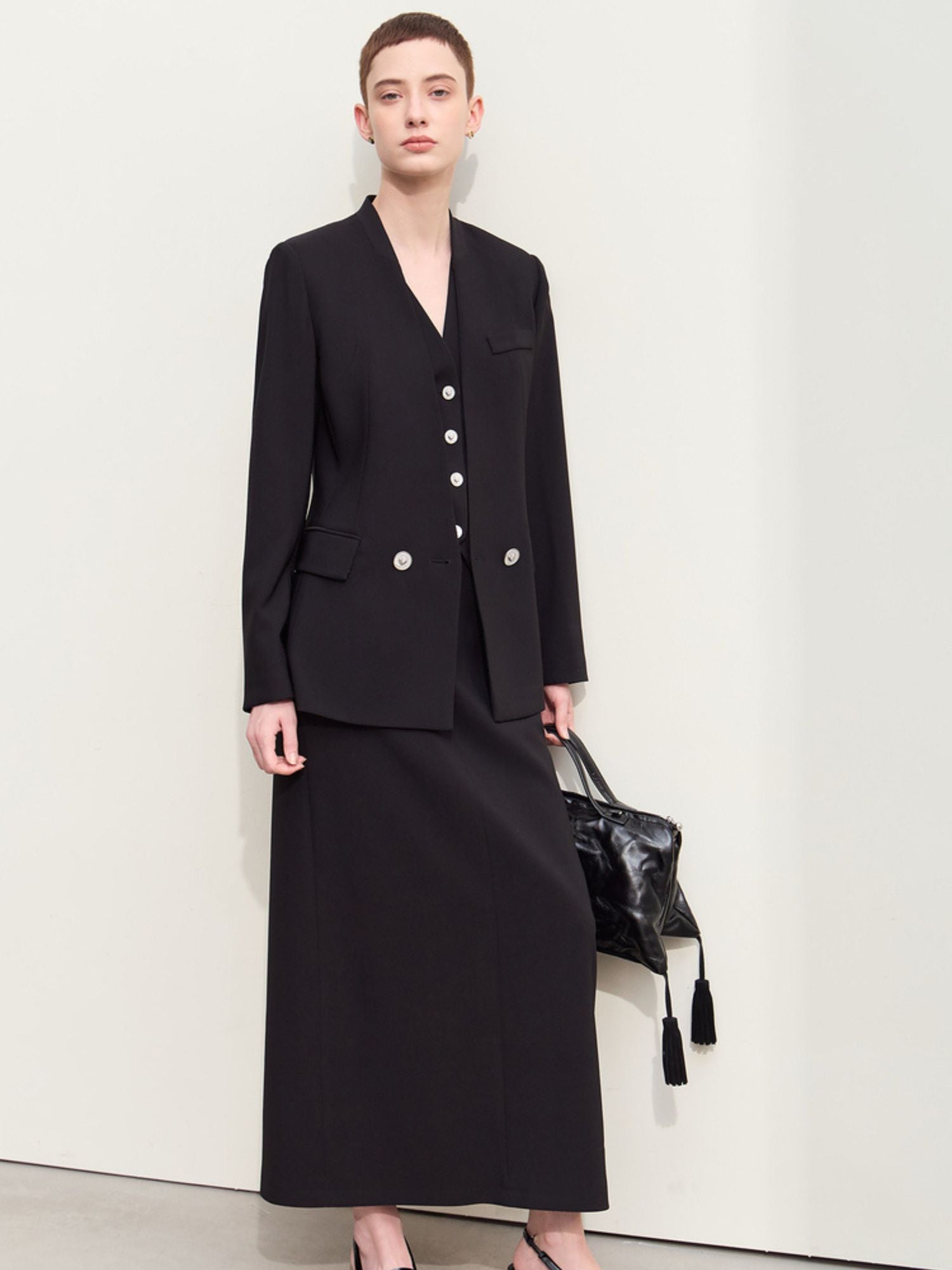 Model wearing a black double-breasted blazer with silver buttons and a matching skirt with a black handbag