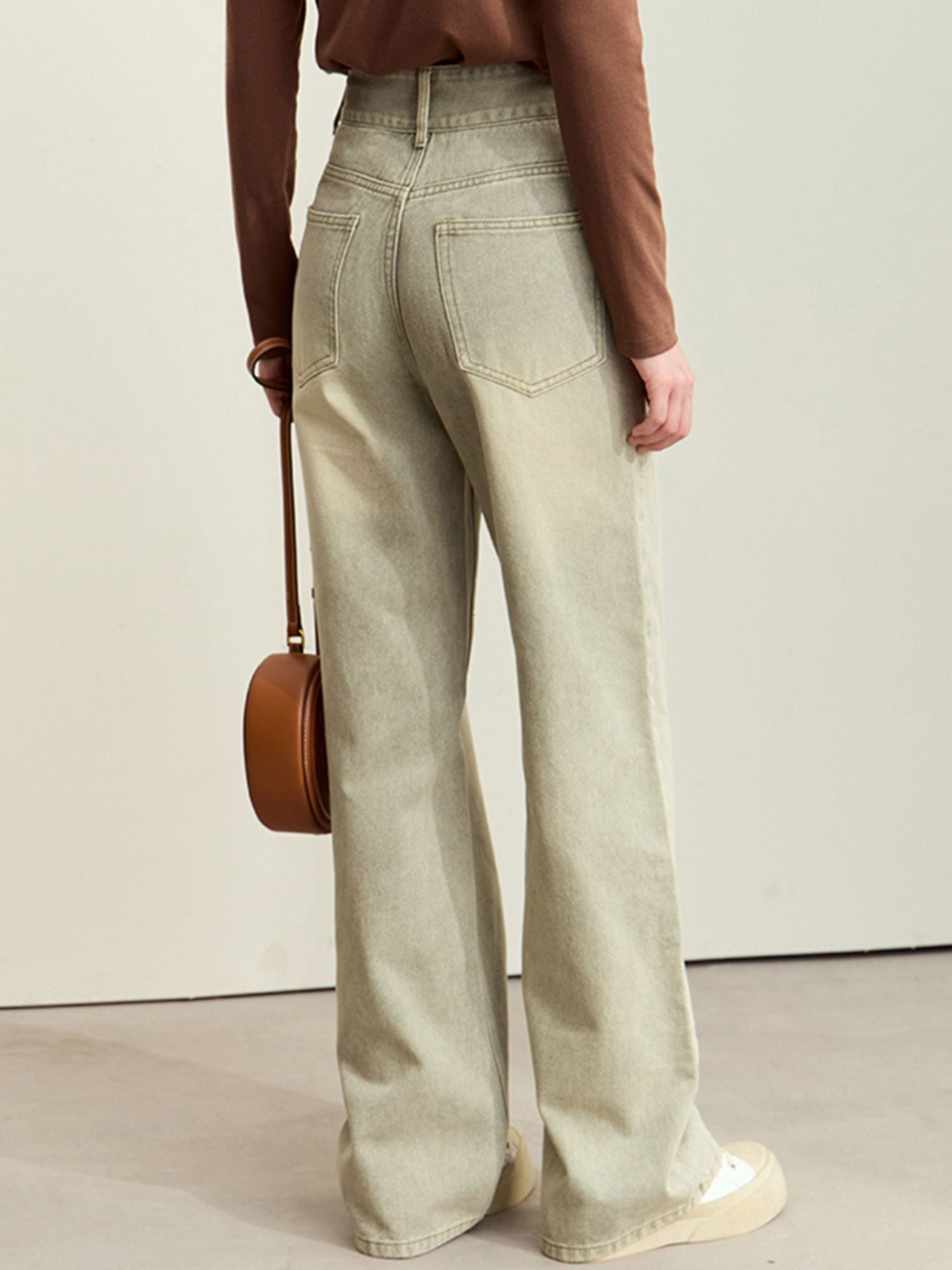 Side view of light-wash wide-leg jeans paired with a brown top and a tan crossbody bag