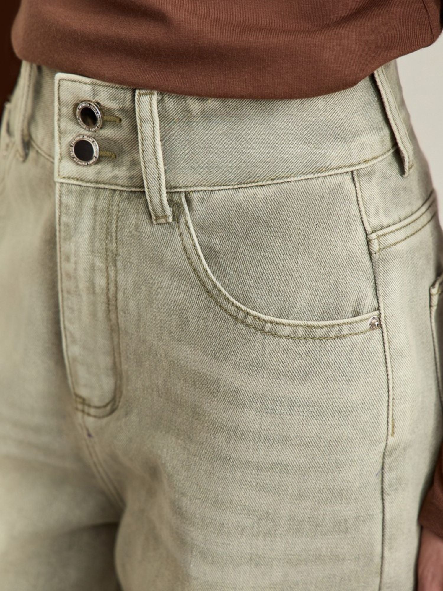 Close-up of waistband and pocket details on light-wash jeans, highlighting the stitching and button closure