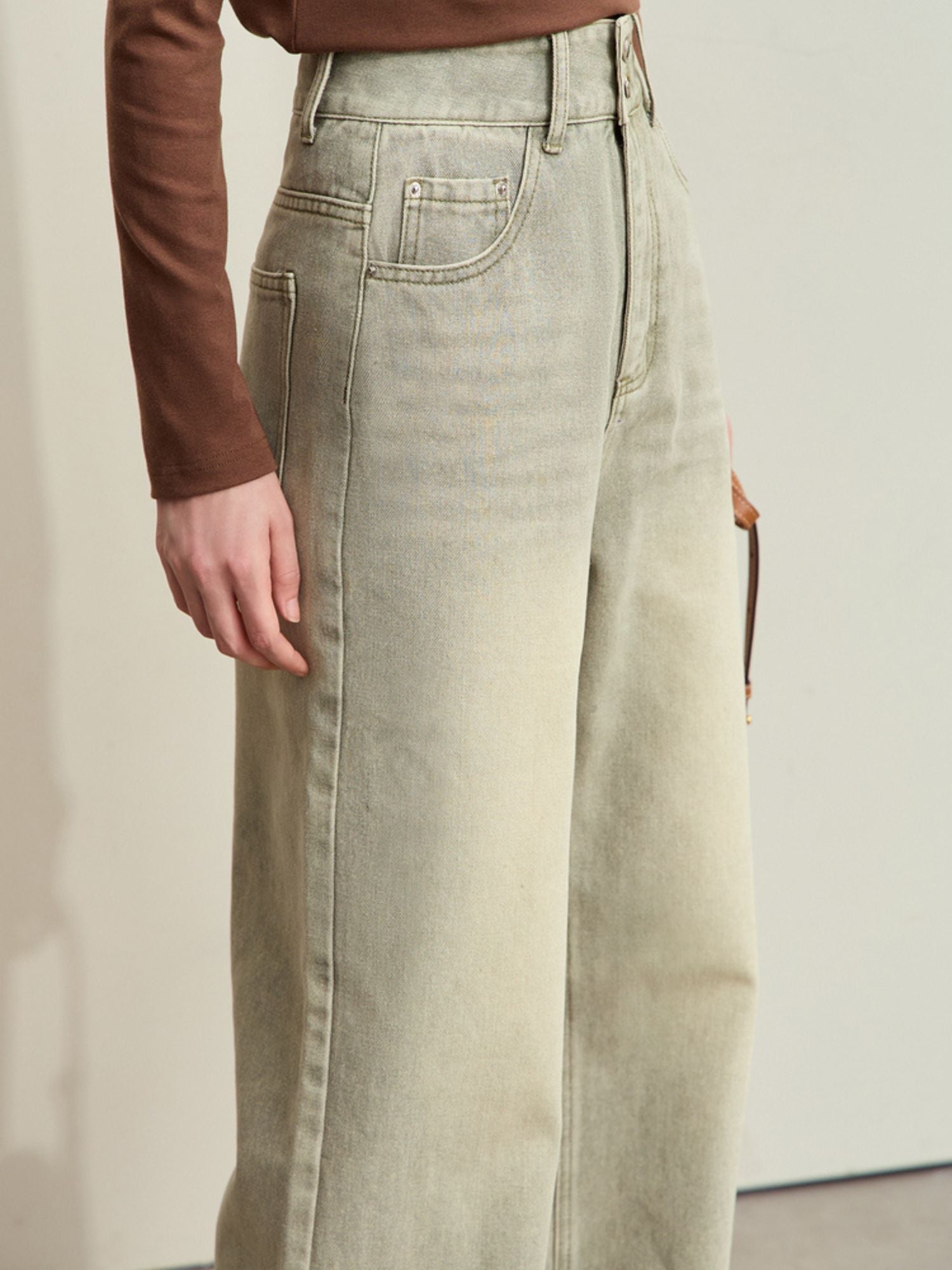 Side view of light-wash jeans with a relaxed fit, paired with a brown long-sleeve top