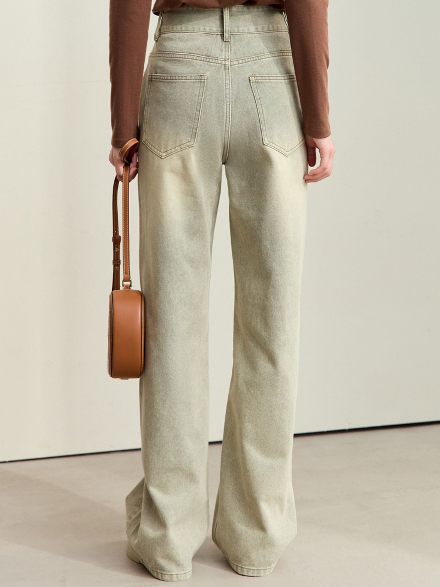 Back view of a person in wide-leg jeans with a brown top, holding a tan crossbody bag