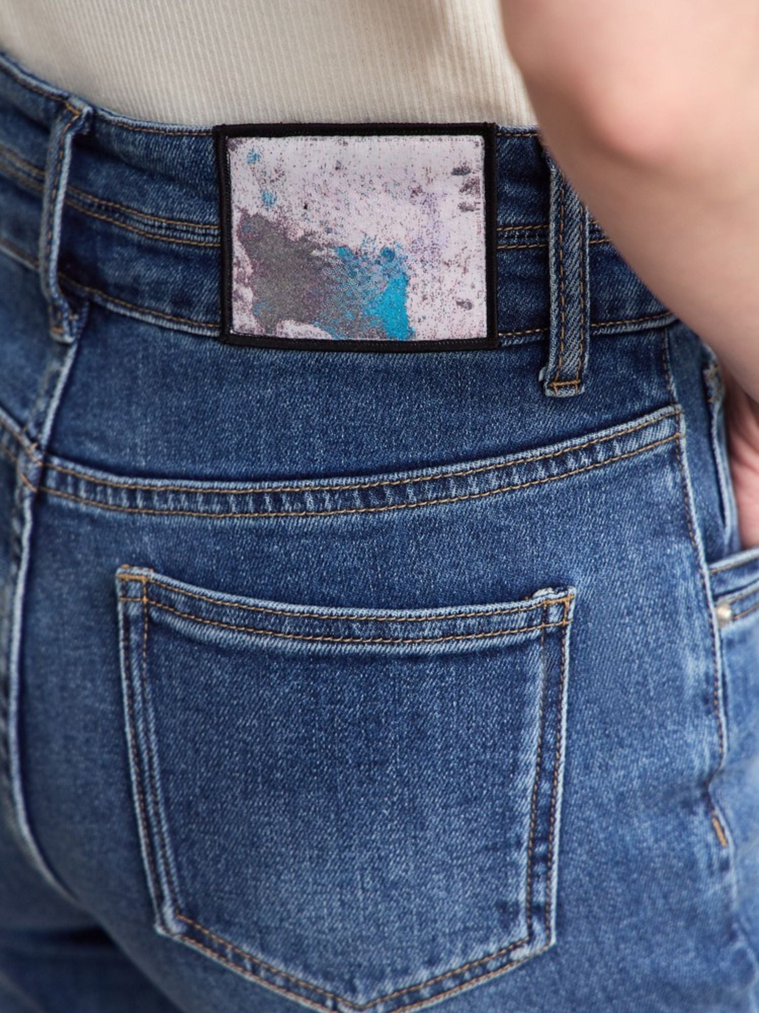 Rear view of a person wearing flared blue jeans, showing the back pockets and hem detail