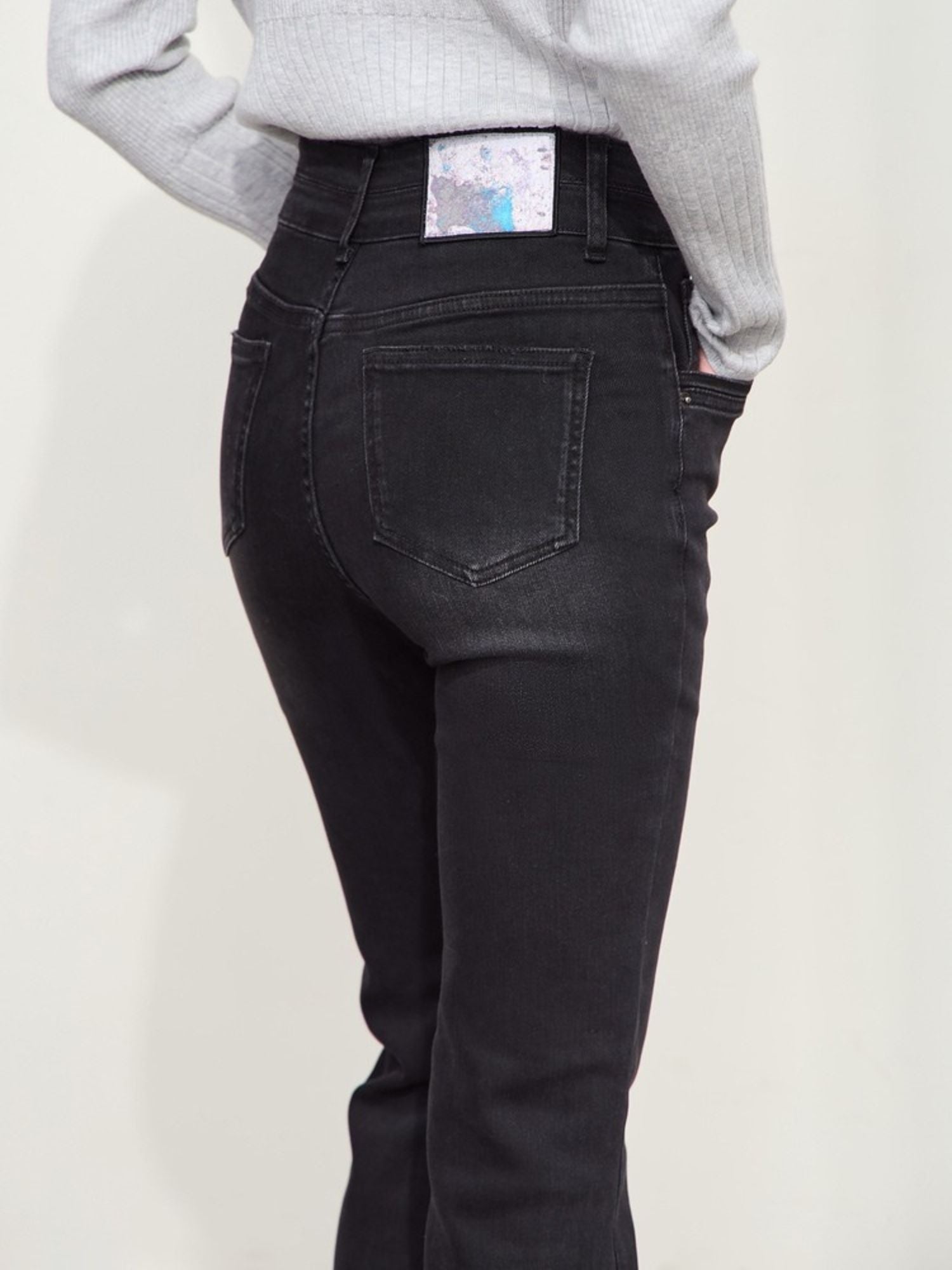 Rear view of a person wearing flared black jeans, showing the back pockets and hem detail