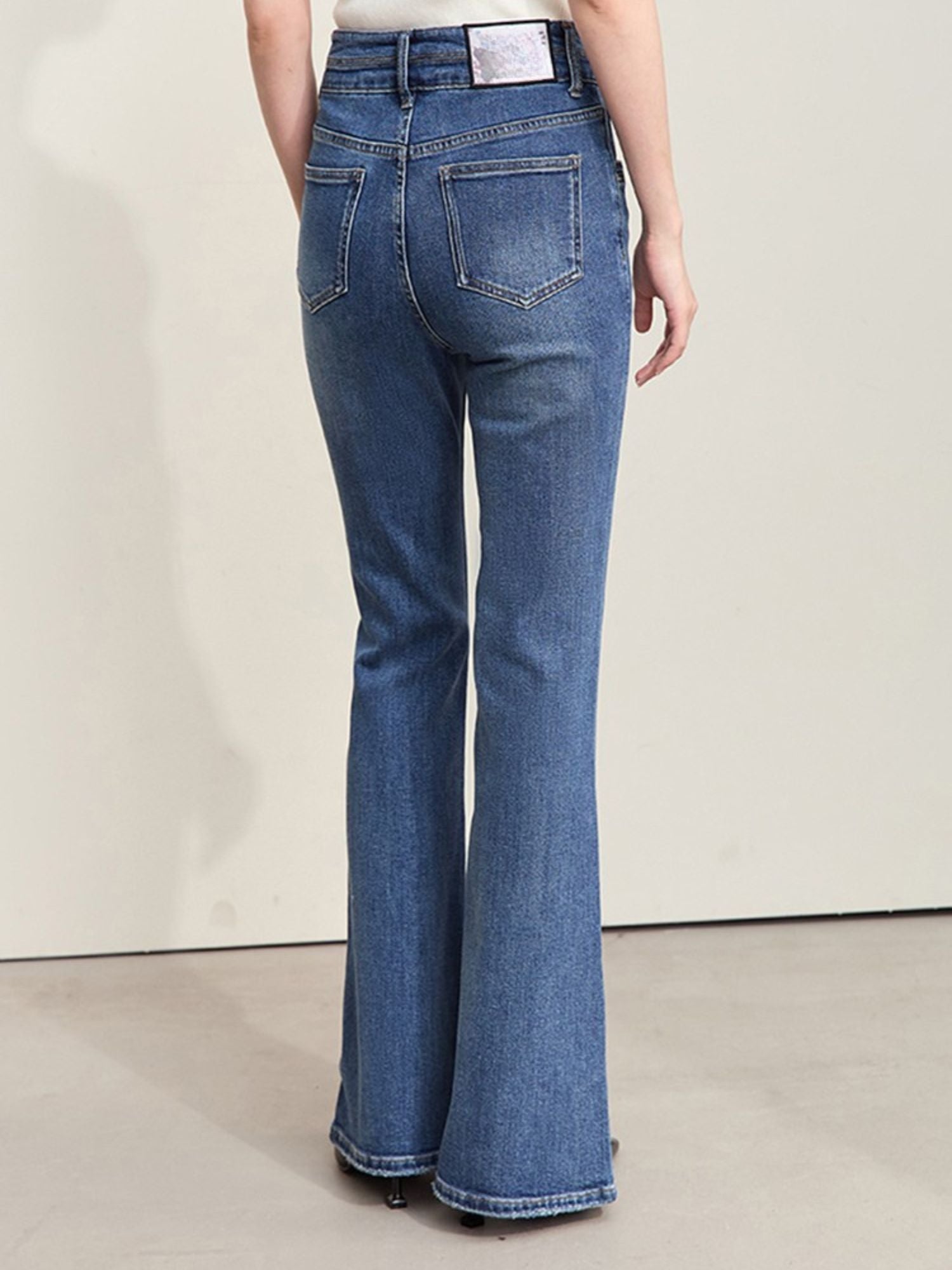 Close-up of the back pocket and waistband of flared blue jeans, showing a rectangular artistic label on the waistband