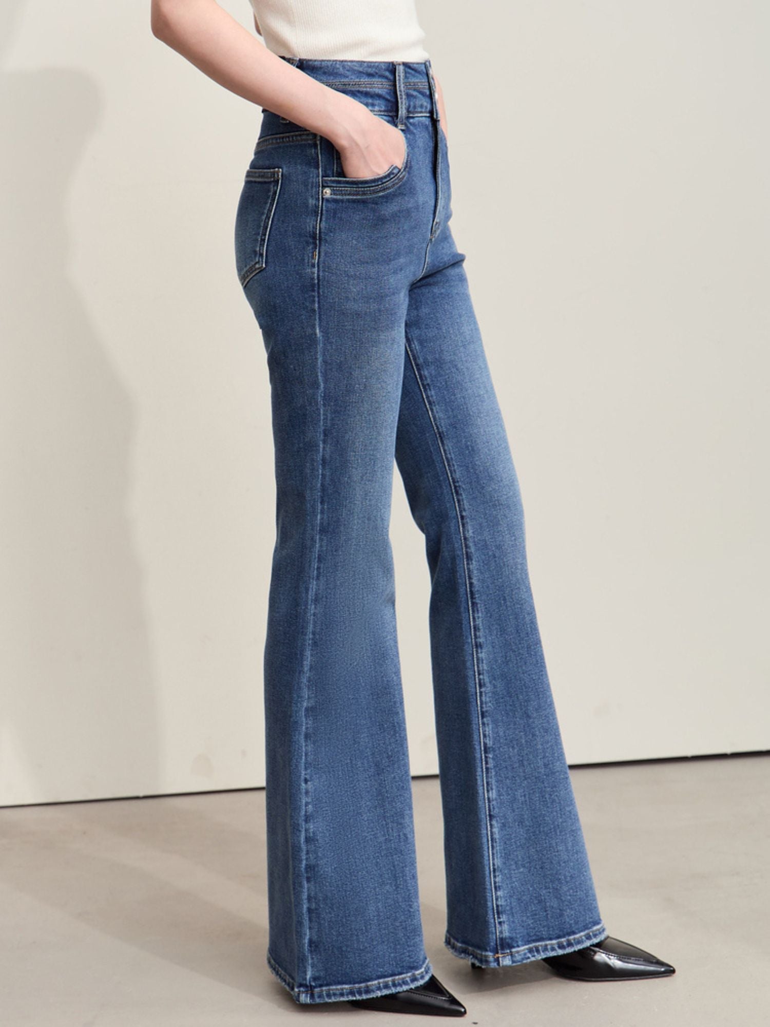 Full-body view of a model wearing flared blue jeans and a black ribbed sweater, holding a black handbag and wearing sunglasses