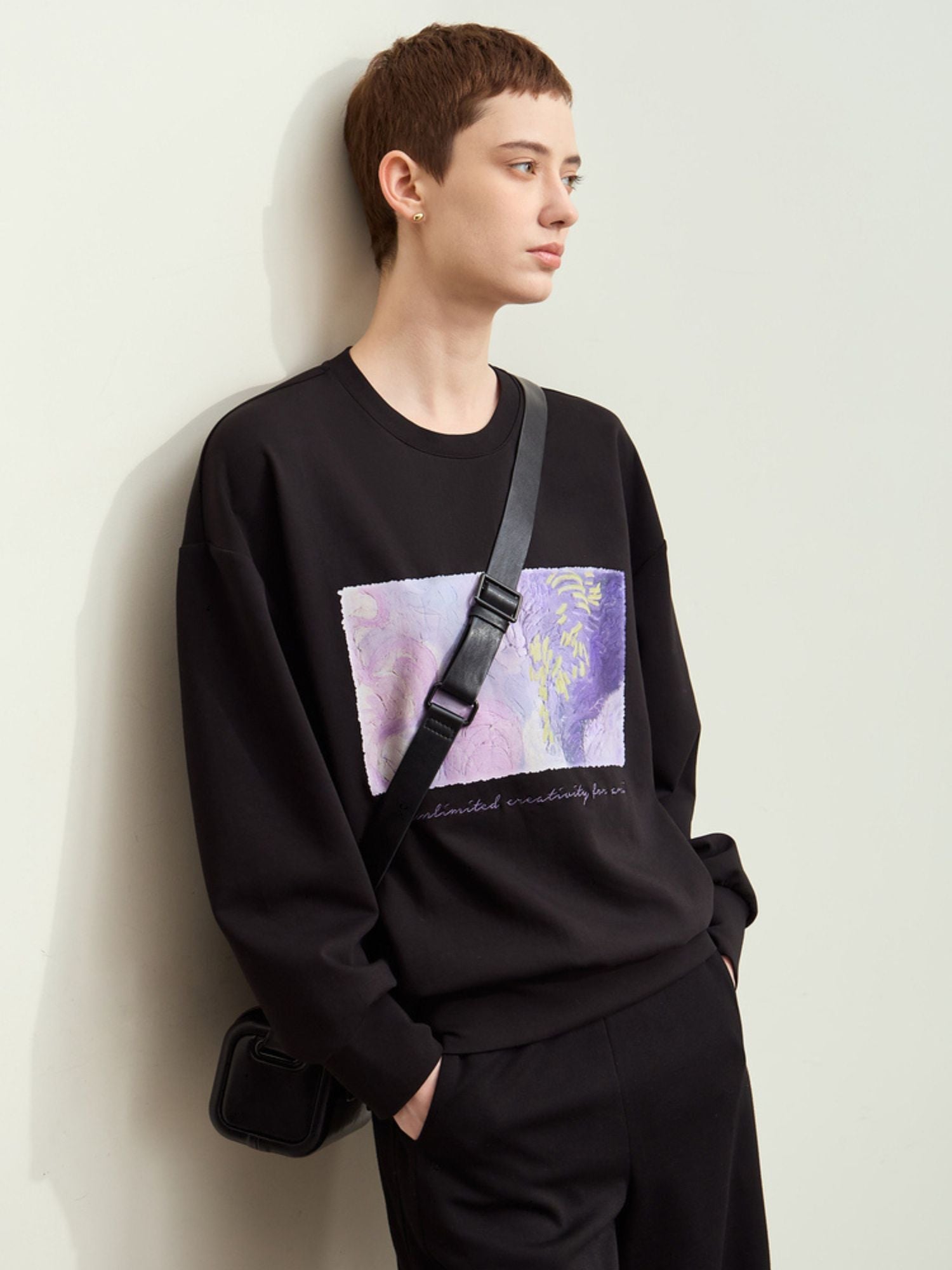 Side view of model in black graphic sweatshirt and black pants, showing sleeve length and drape