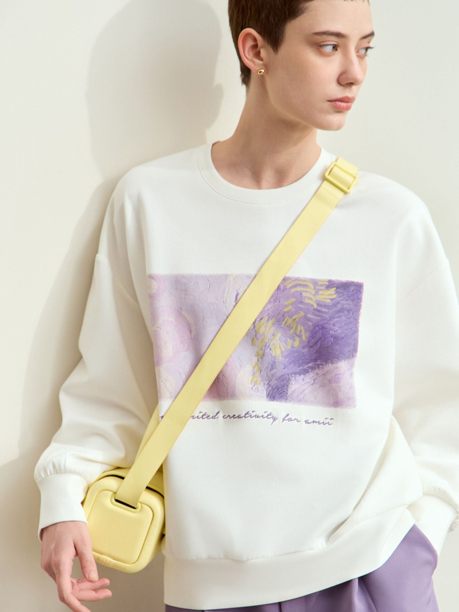 Three-quarter front view of white graphic sweatshirt with lavender shorts, accessorized with yellow bag