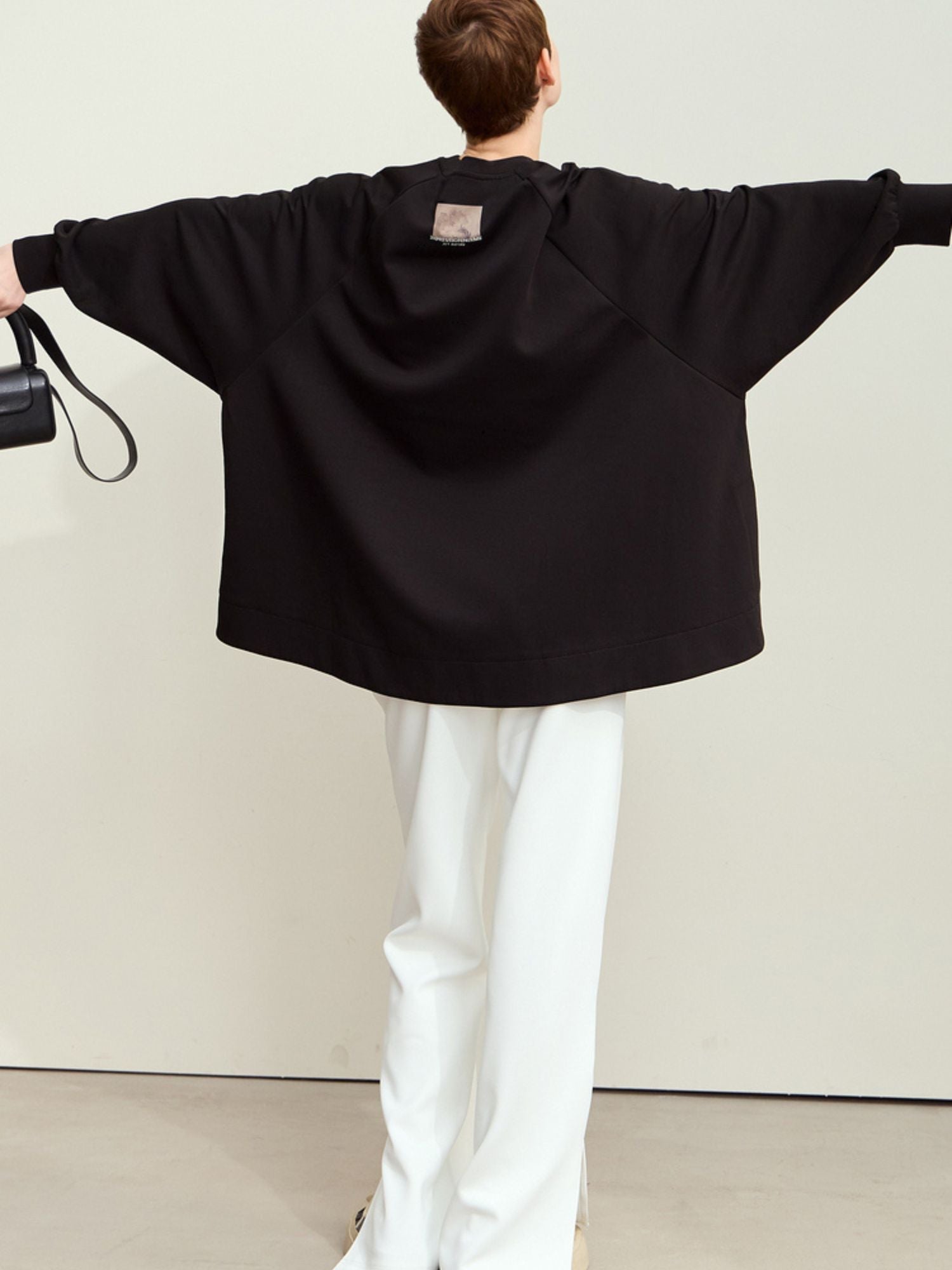Back view of model in black oversized sweatshirt, arms fully extended to the sides