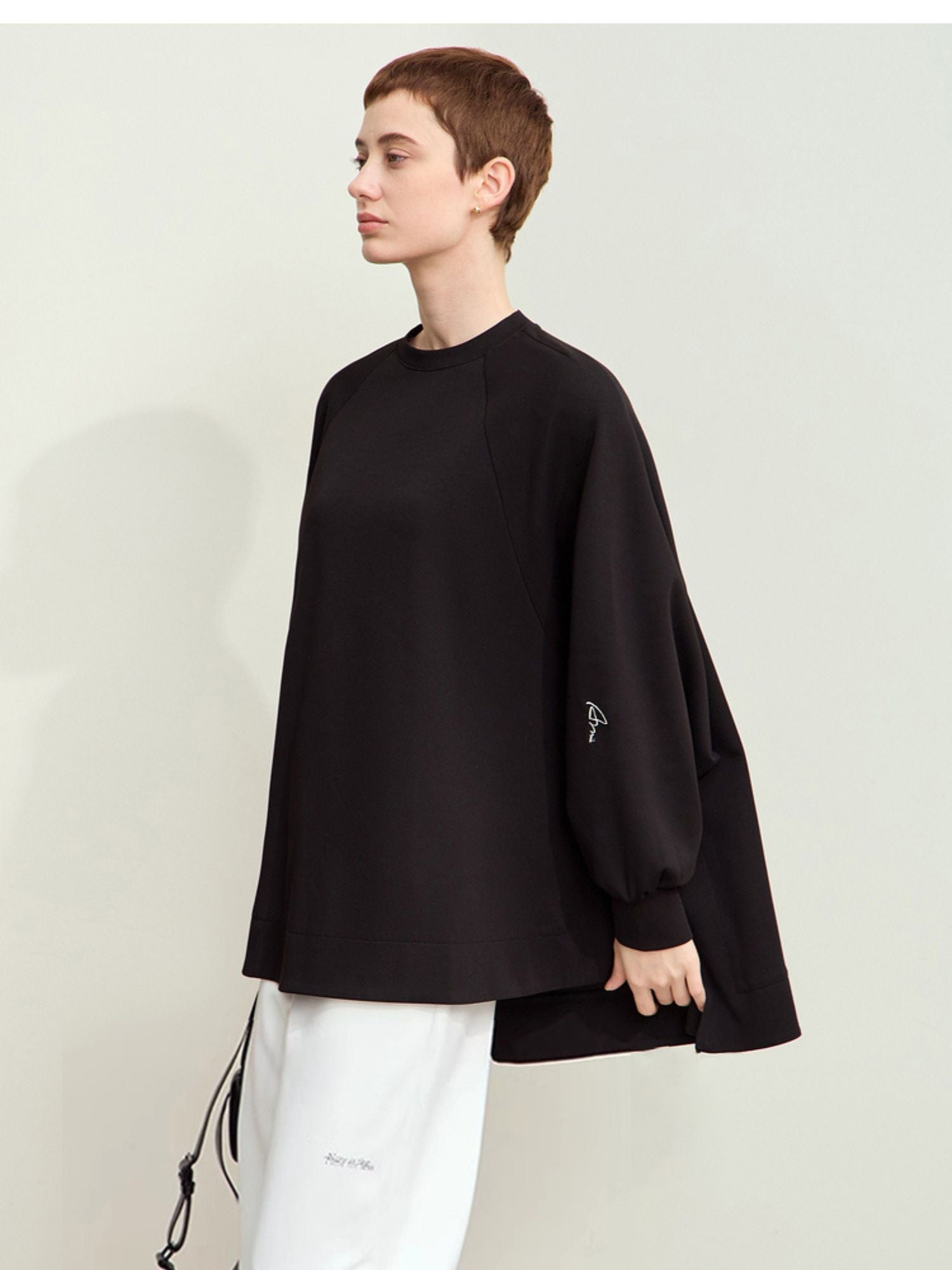 Three-quarter view of model in black oversized sweatshirt and white pants, standing facing forward