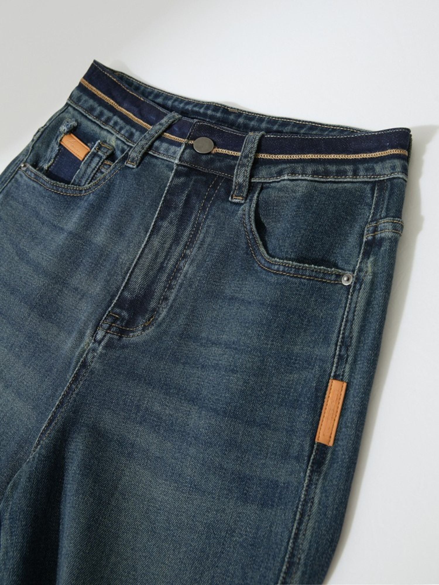 Close-up front view of straight-leg blue jeans, showing the waistband, zipper, and front pocket detail with a brown leather tag