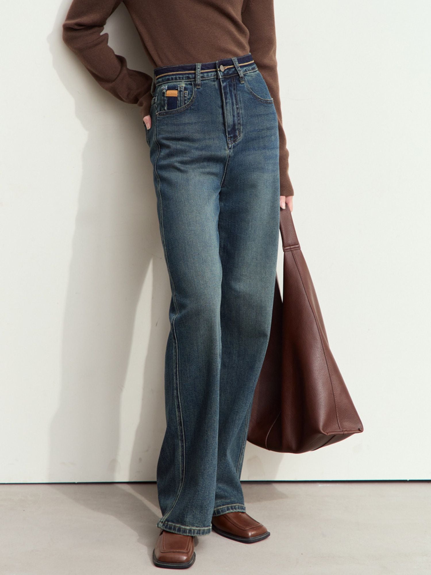 Three-quarter side view of a person wearing straight-leg jeans and a beige sweater, standing against a plain wall