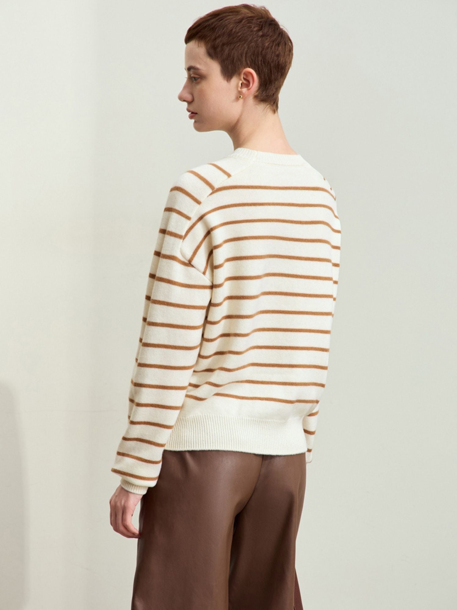 Rear three-quarter view of model in beige-striped sweater, showing back fit