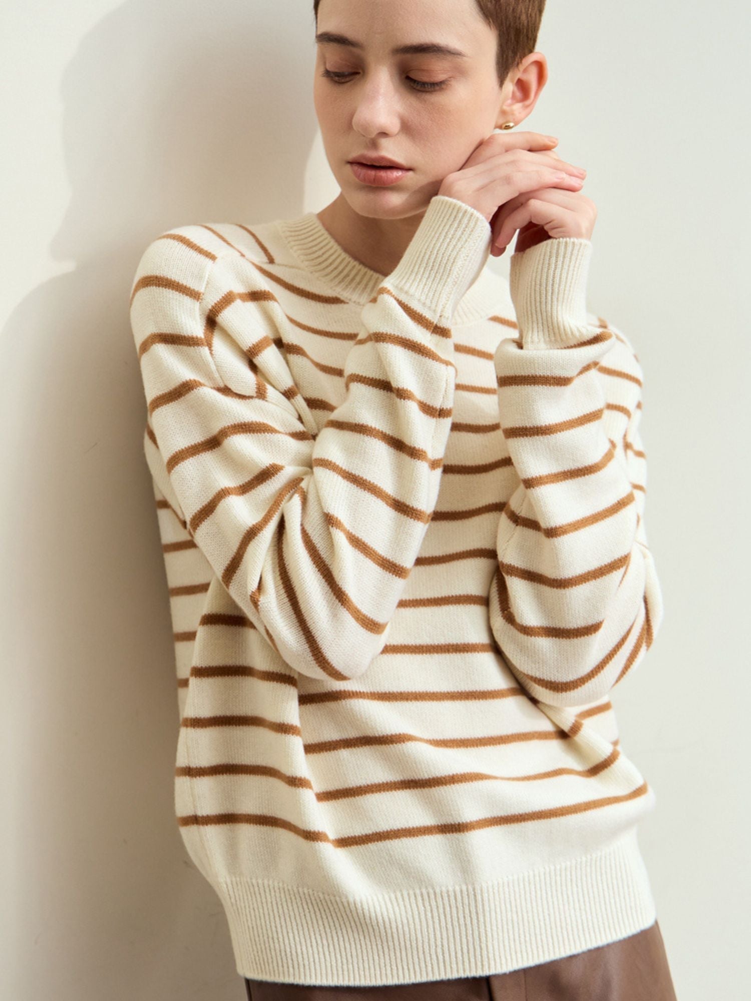 Close-up side view of the model’s upper body in the cream-and-camel striped sweater, hand touching chin