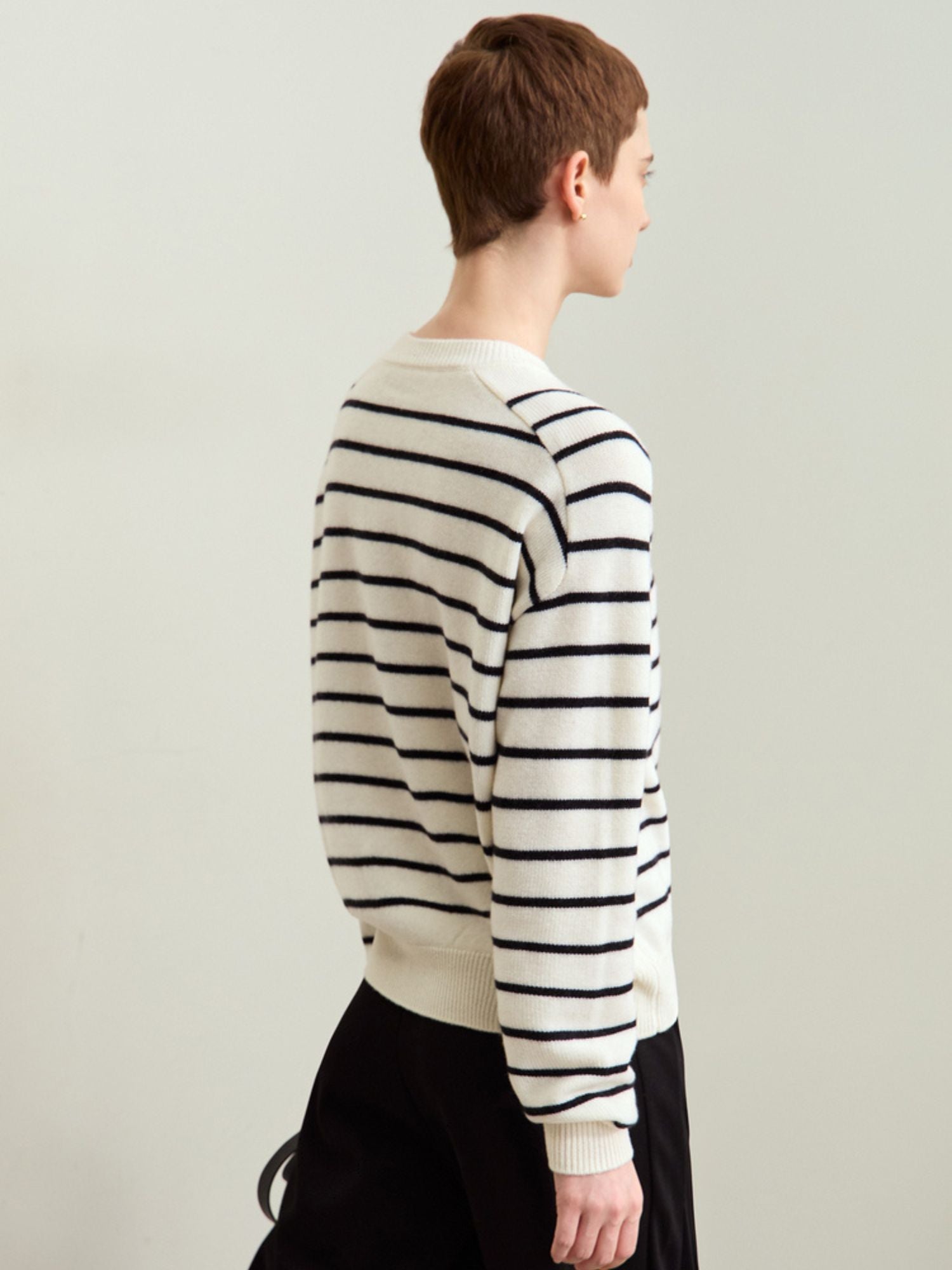 Rear three-quarter view of model in black-striped sweater, showing back fit.
