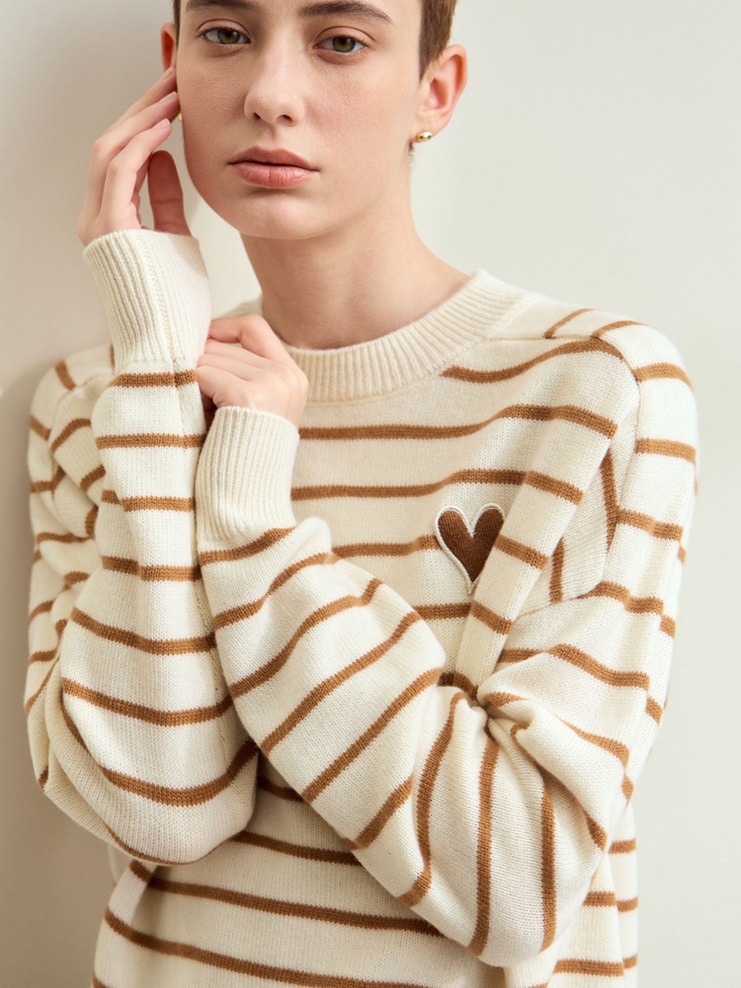 Close-up of model’s face and upper torso in the beige-striped sweater, hand resting on chin