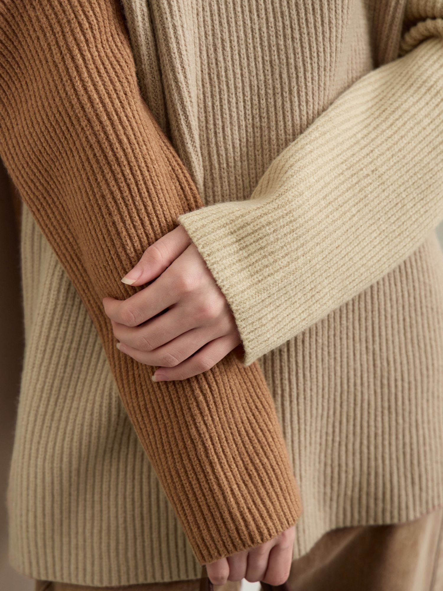 Close-up of hand touching beige and cream color-block sleeve to show knit rib detail