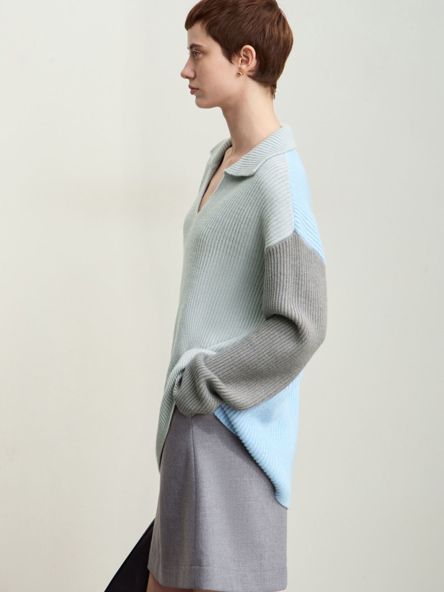 Three-quarter front view of model wearing the sweater paired with a skirt, standing facing left