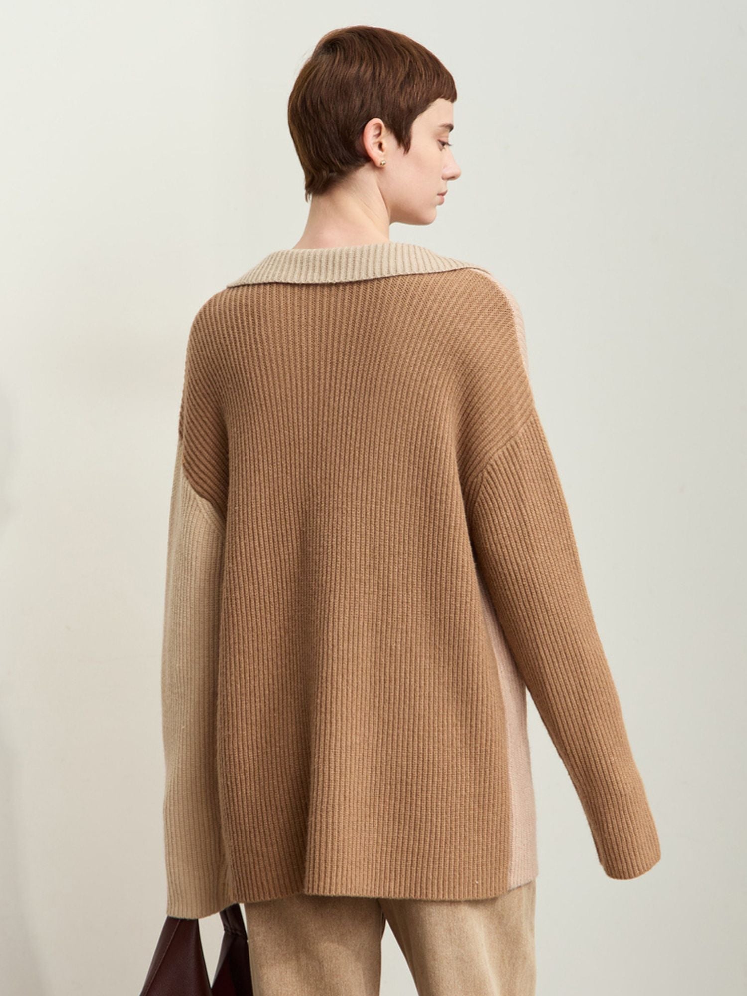 Rear three-quarter view of model in beige/cream sweater standing against wall