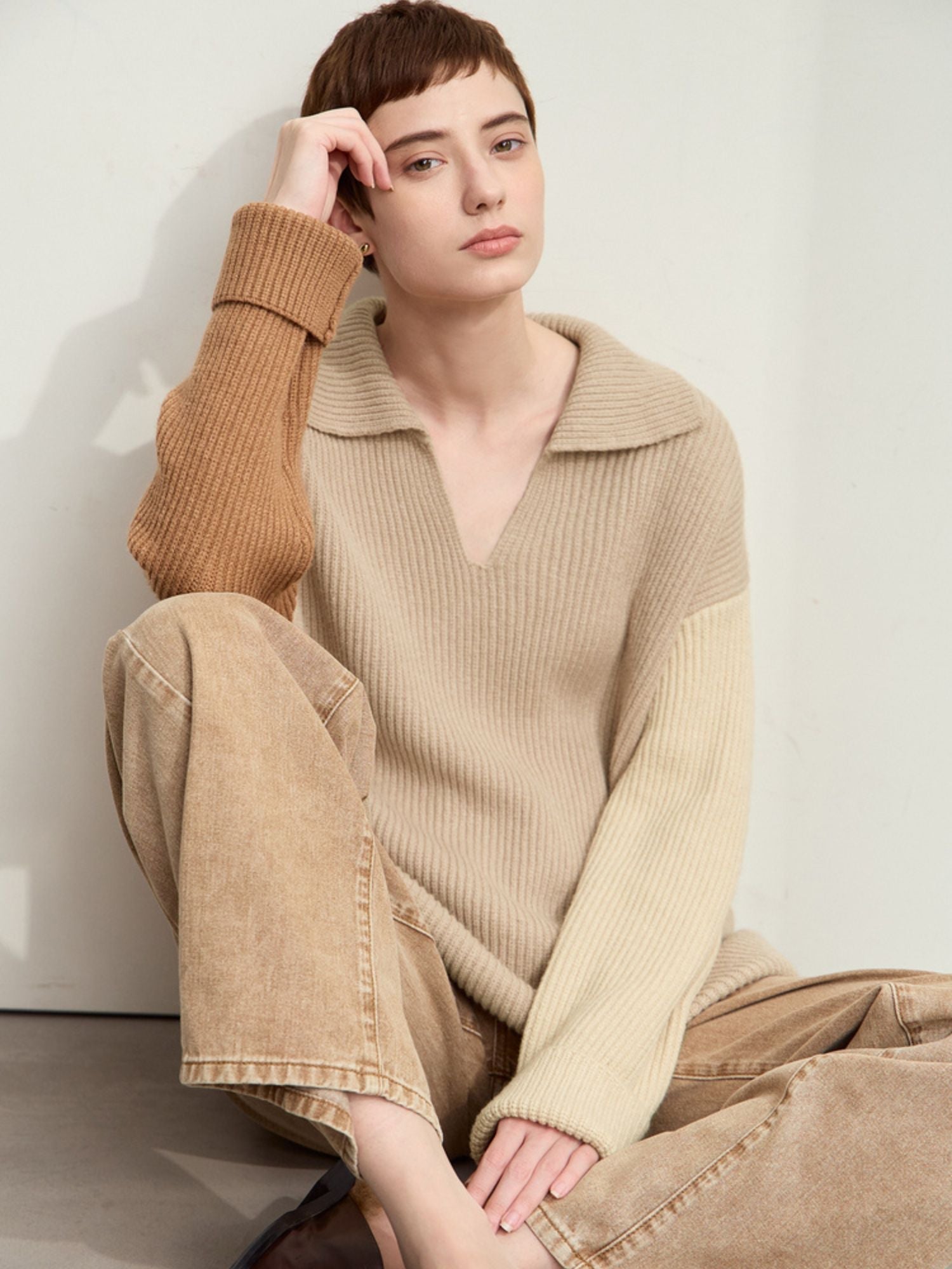 Model wearing beige and cream color-block sweater in seated pose