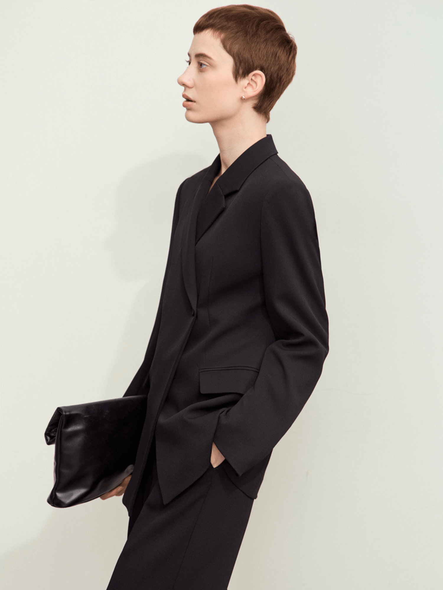 Side view of black tailored blazer with structured shoulders and a black handbag