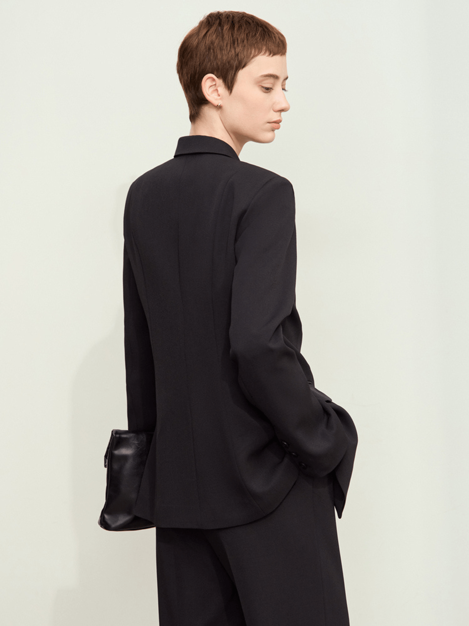 Side/back view of black blazer styled with black trousers and black handbag, highlighting silhouette