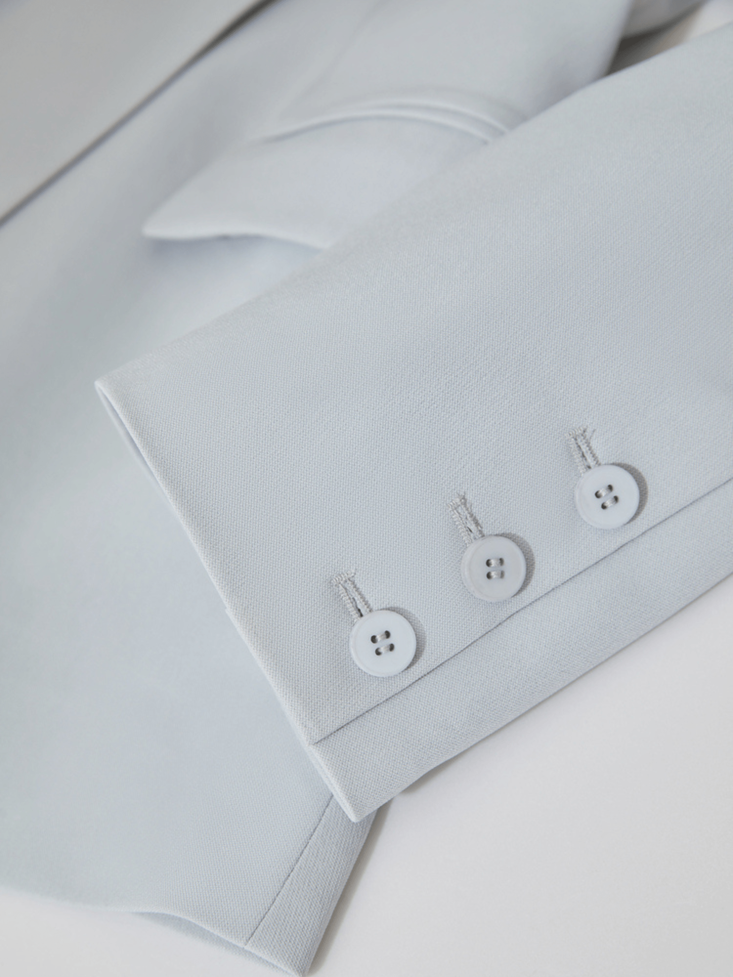 Close‑up of light‑blue blazer cuff with three tonal buttons