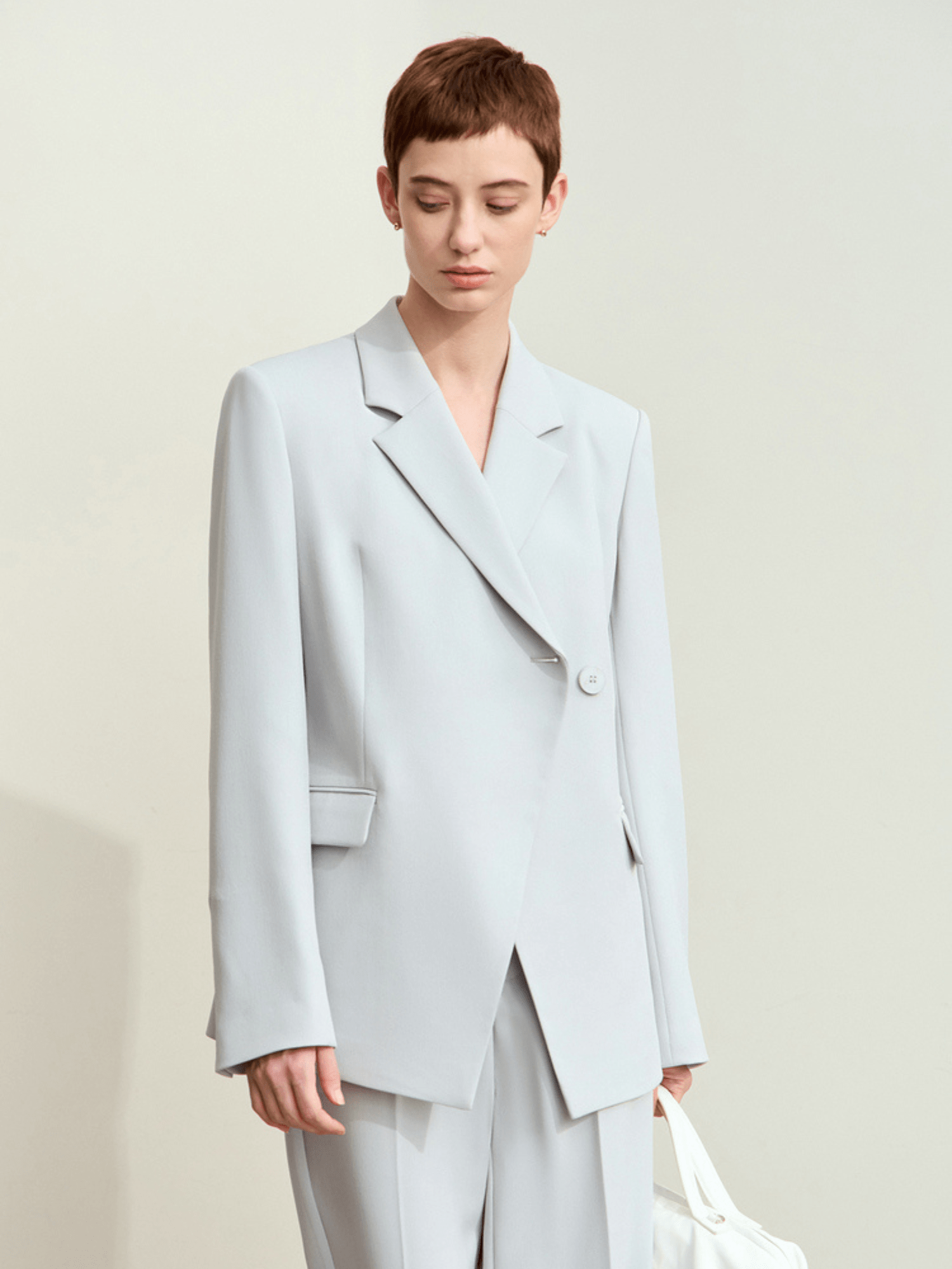 Front view of light‑blue tailored blazer with structured shoulders with trousers and white handbag