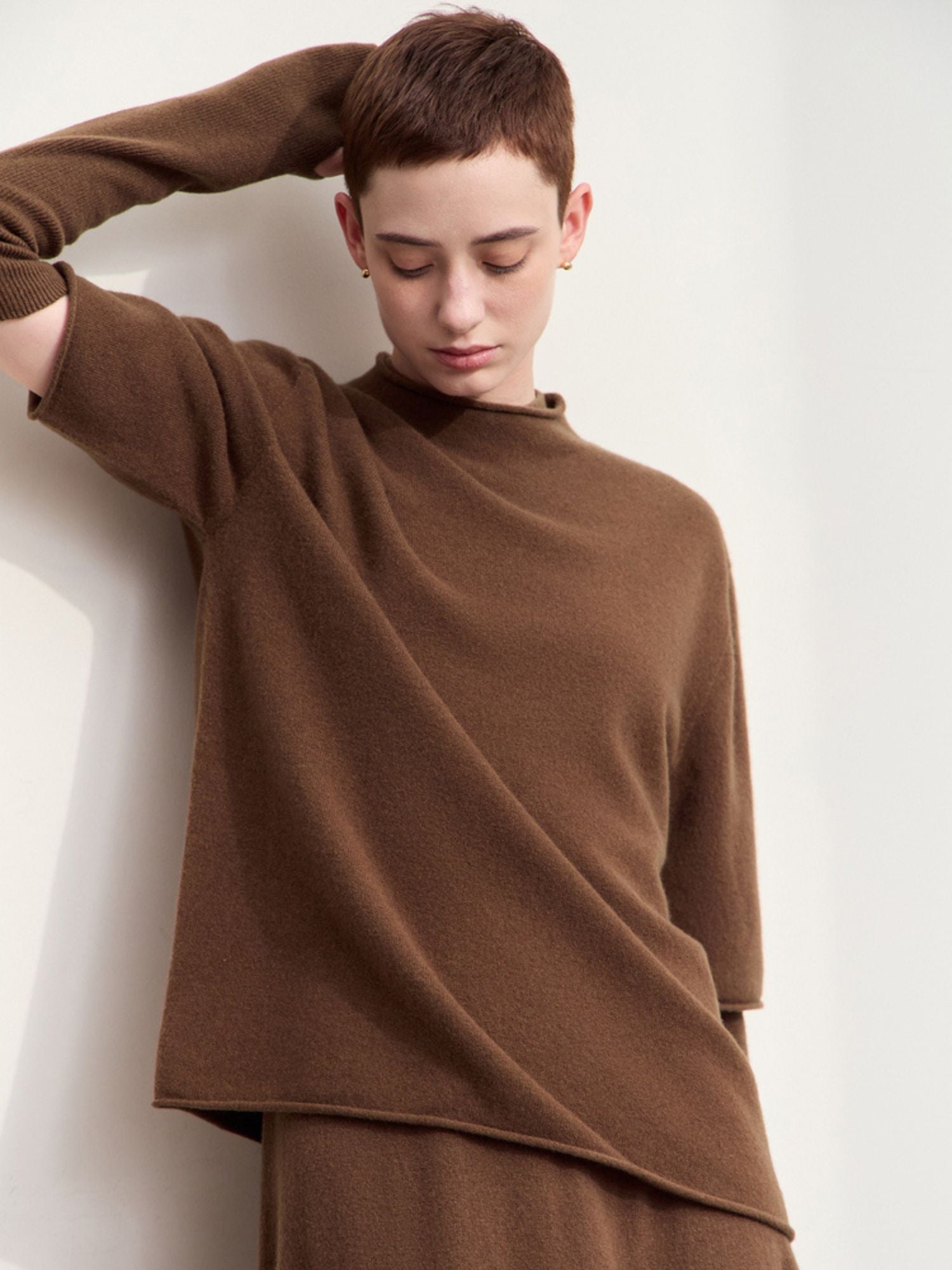 Model lifting arm in oversized brown sweater, showing draped fit and slit detail