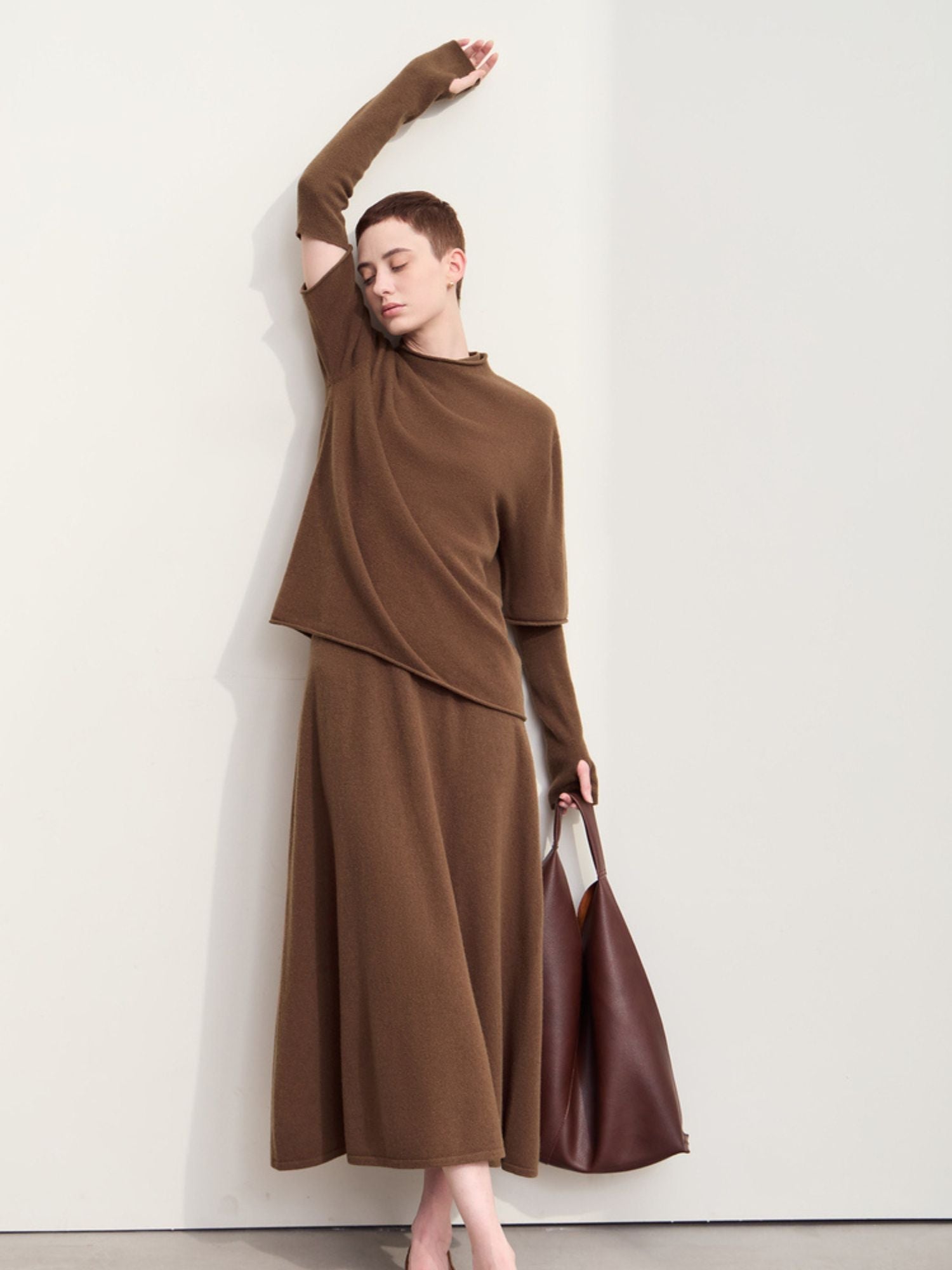 Full-body view of model in brown sweater and skirt, hand raised above head