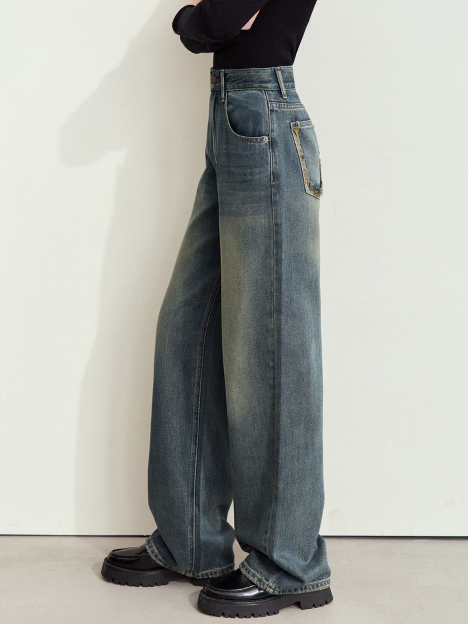 Side view of wide-leg blue jeans worn with a sleeveless black top and black shoes