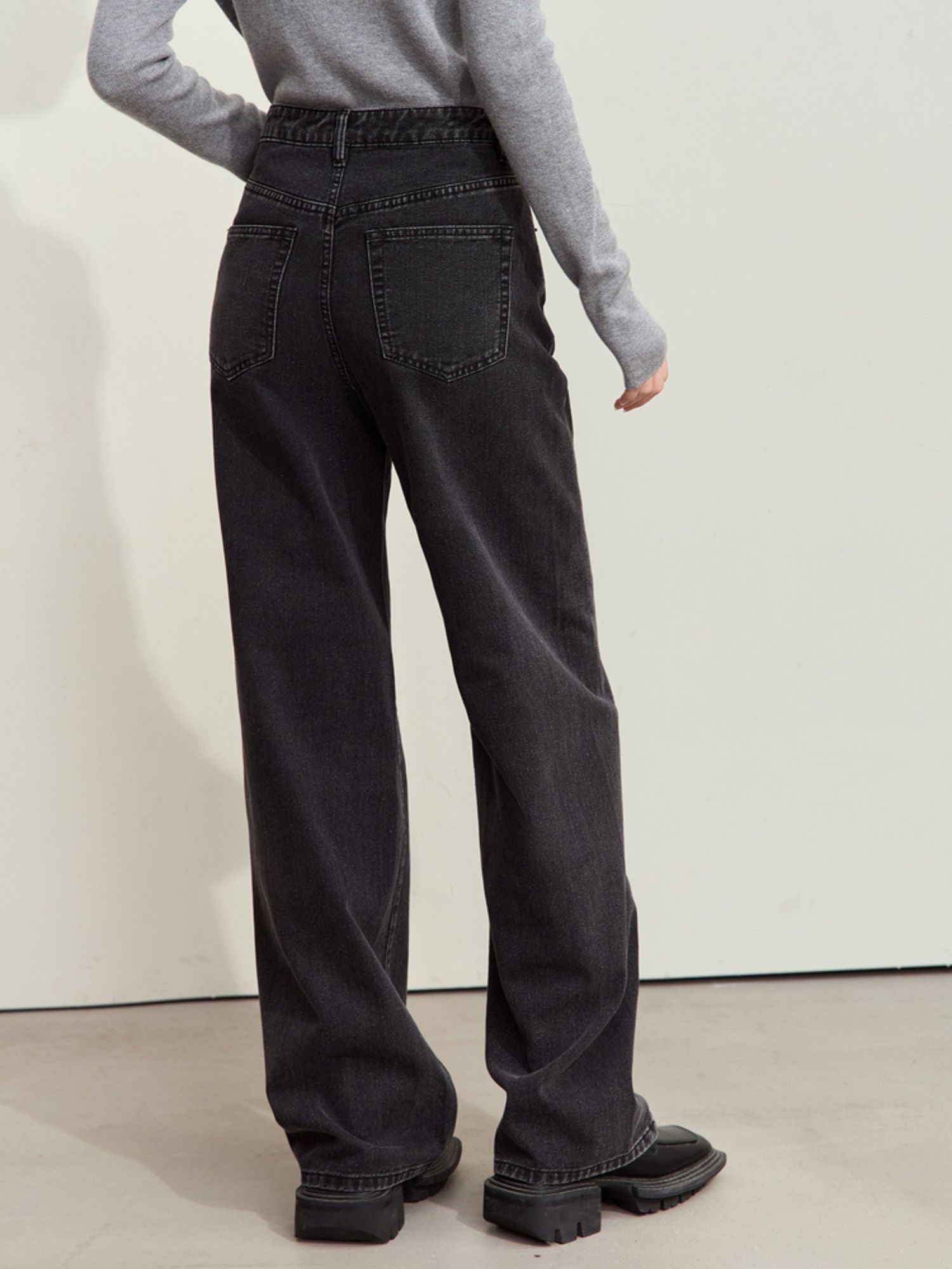 Three-quarter side view of black wide-leg corduroy pants styled with a grey ribbed sweater and black shoes