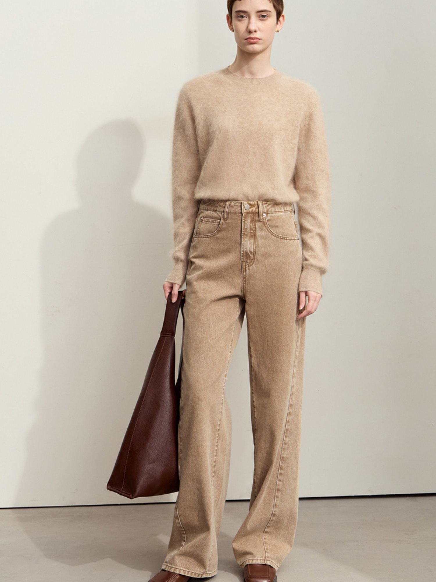 Front view of a person in tan corduroy pants and a beige sweater, standing casually with a brown bag